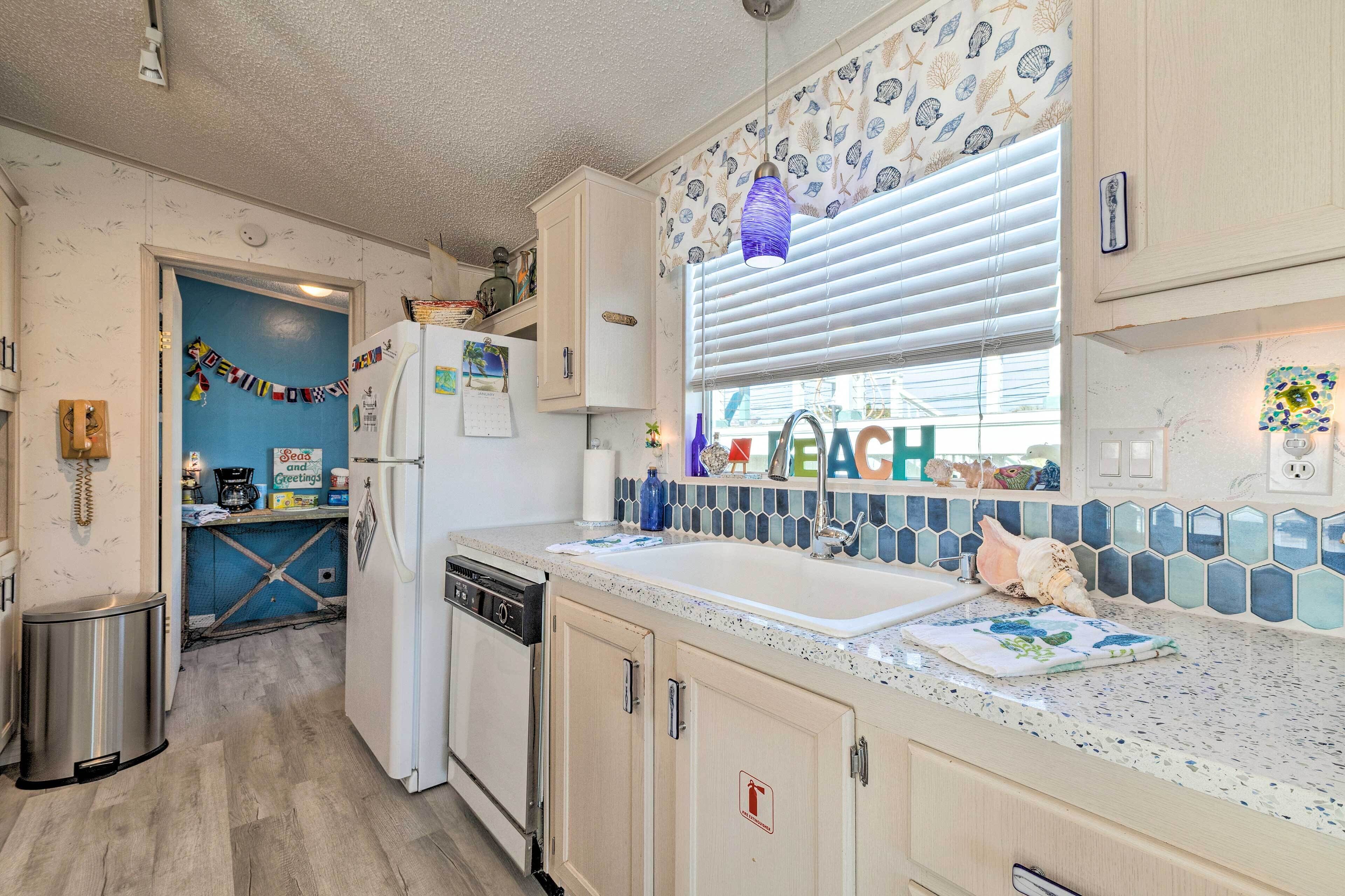 A compact kitchen with a built-in dishwasher, a refrigerator with magnets, and a window with blinds.
