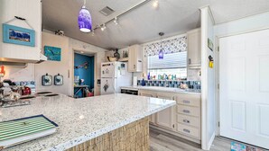 A modern kitchen with a granite countertop, white cabinets, and a hanging pendant light. - Elevated Deck! Fun-filled Homosassa River Home (Homosassa)
