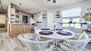 A nautical-themed dining area with round tables, white wicker chairs, and a kitchen in the background. - Elevated Deck! Fun-filled Homosassa River Home (Homosassa)