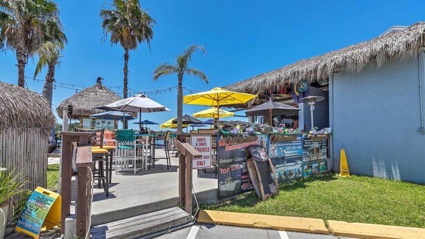 A beachfront restaurant with outdoor seating, palm trees, and thatched-roof structures. - Elevated Deck! Fun-filled Homosassa River Home (Homosassa)