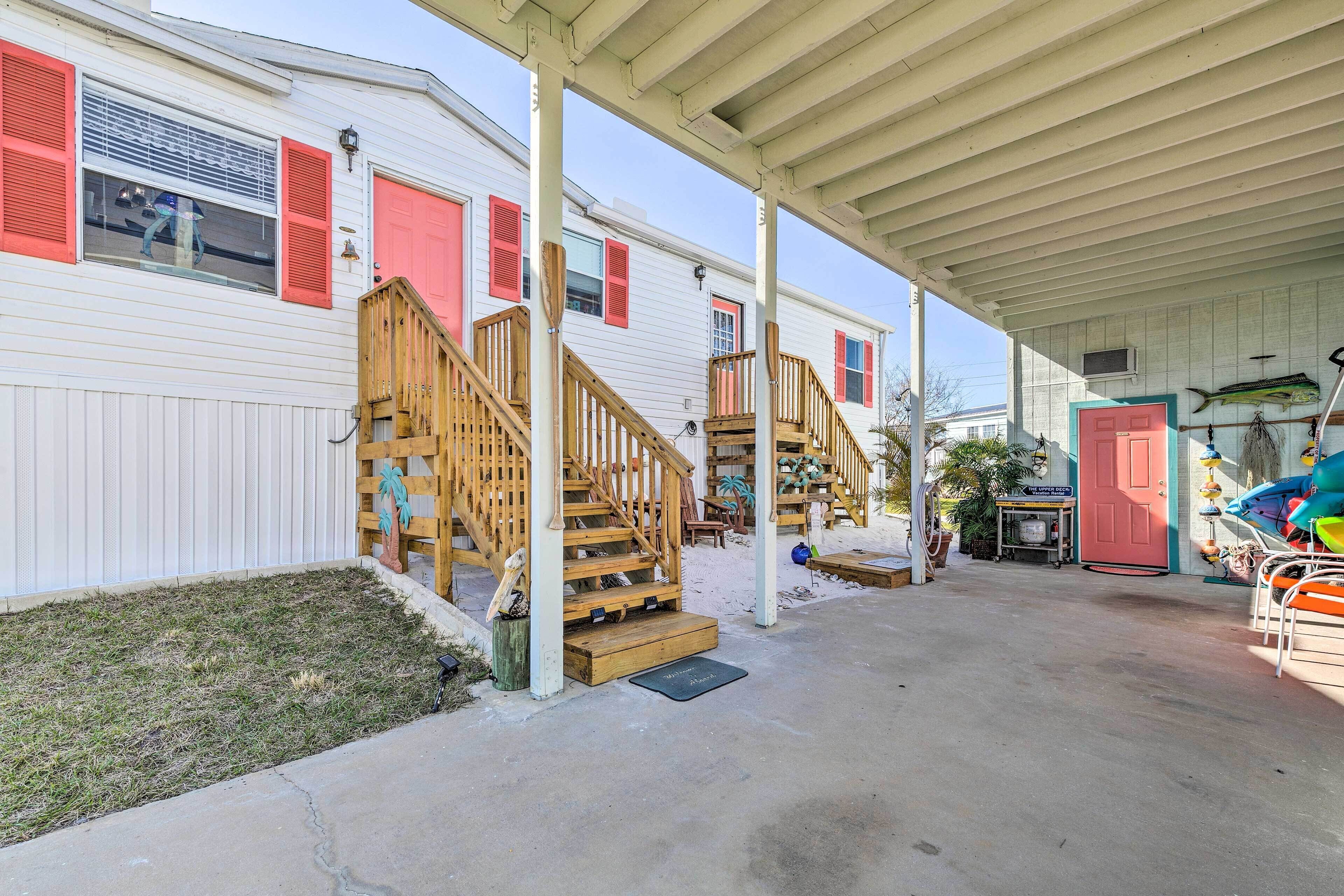 A covered outdoor area with wooden stairs leading to a porch, a red door, and a small table with chairs.