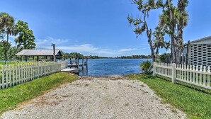A waterfront property with a gravel pathway leading to a dock, surrounded by a white picket fence and palm trees. - Elevated Deck! Fun-filled Homosassa River Home (Homosassa)