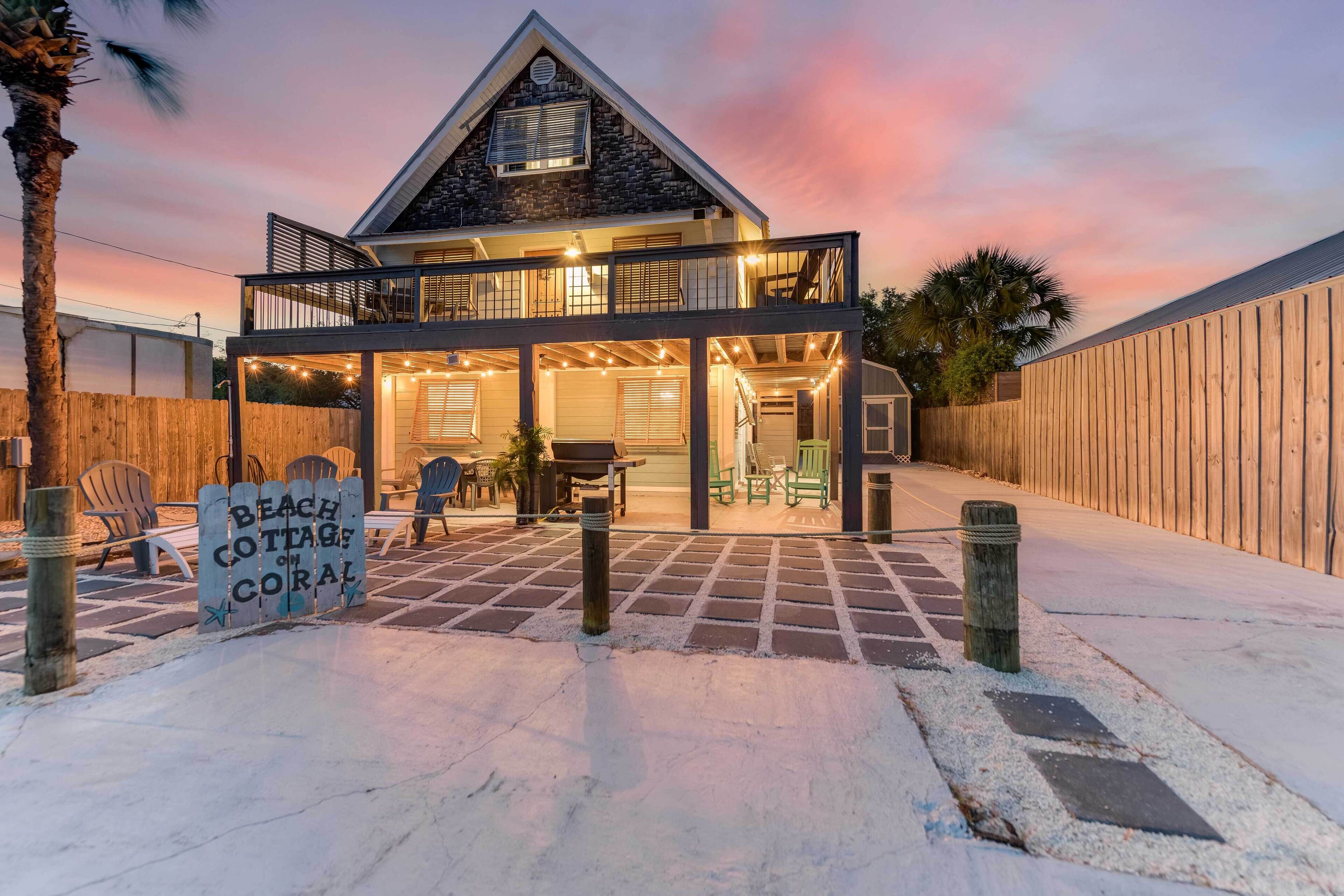 Ein zweistöckiges Strandhaus mit Balkon, einer überdachten Terrasse und einem Schild mit der Aufschrift 'Beach Cottage Coral'.