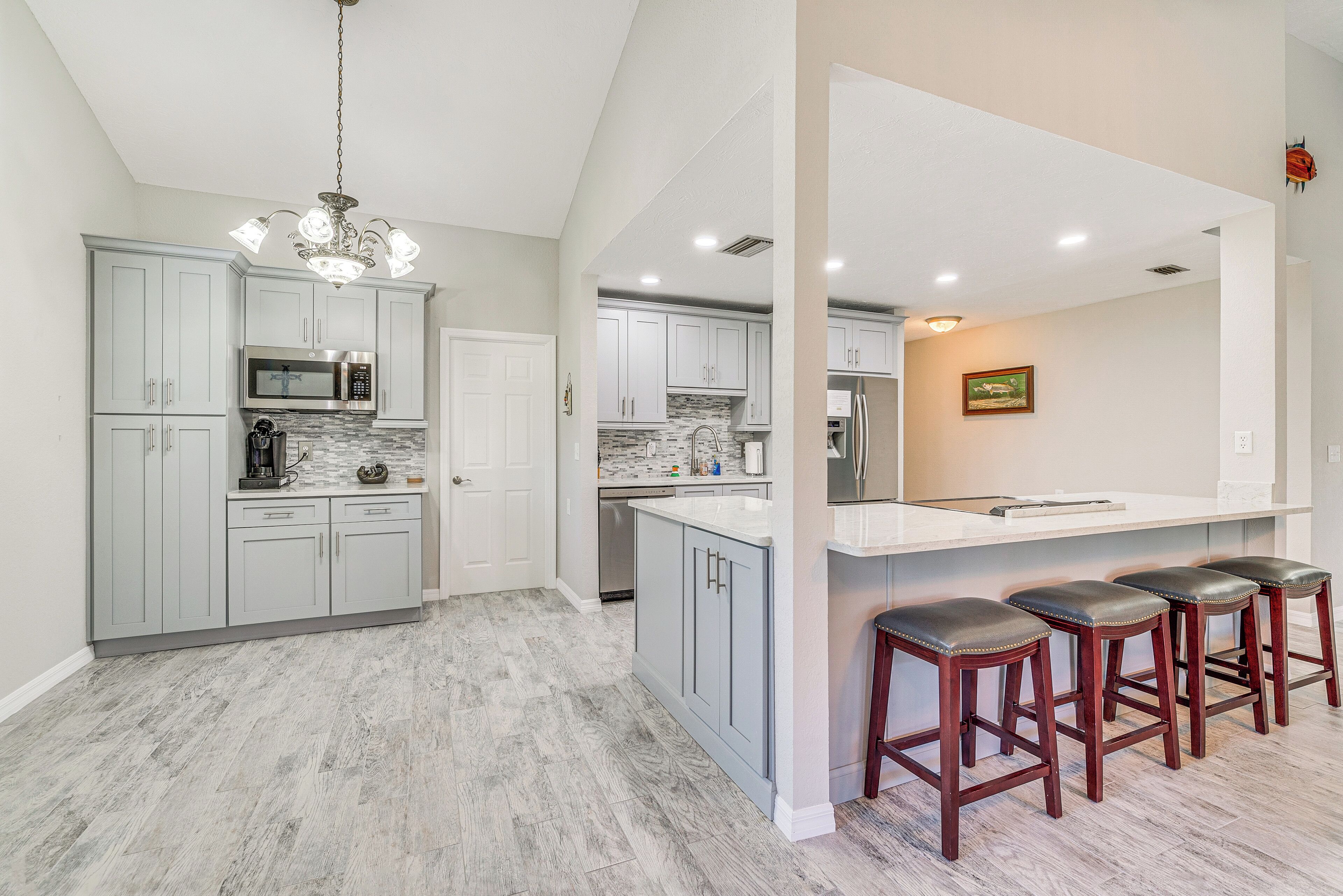 A modern kitchen with grey cabinets, a central island with stools, and a chandelier.