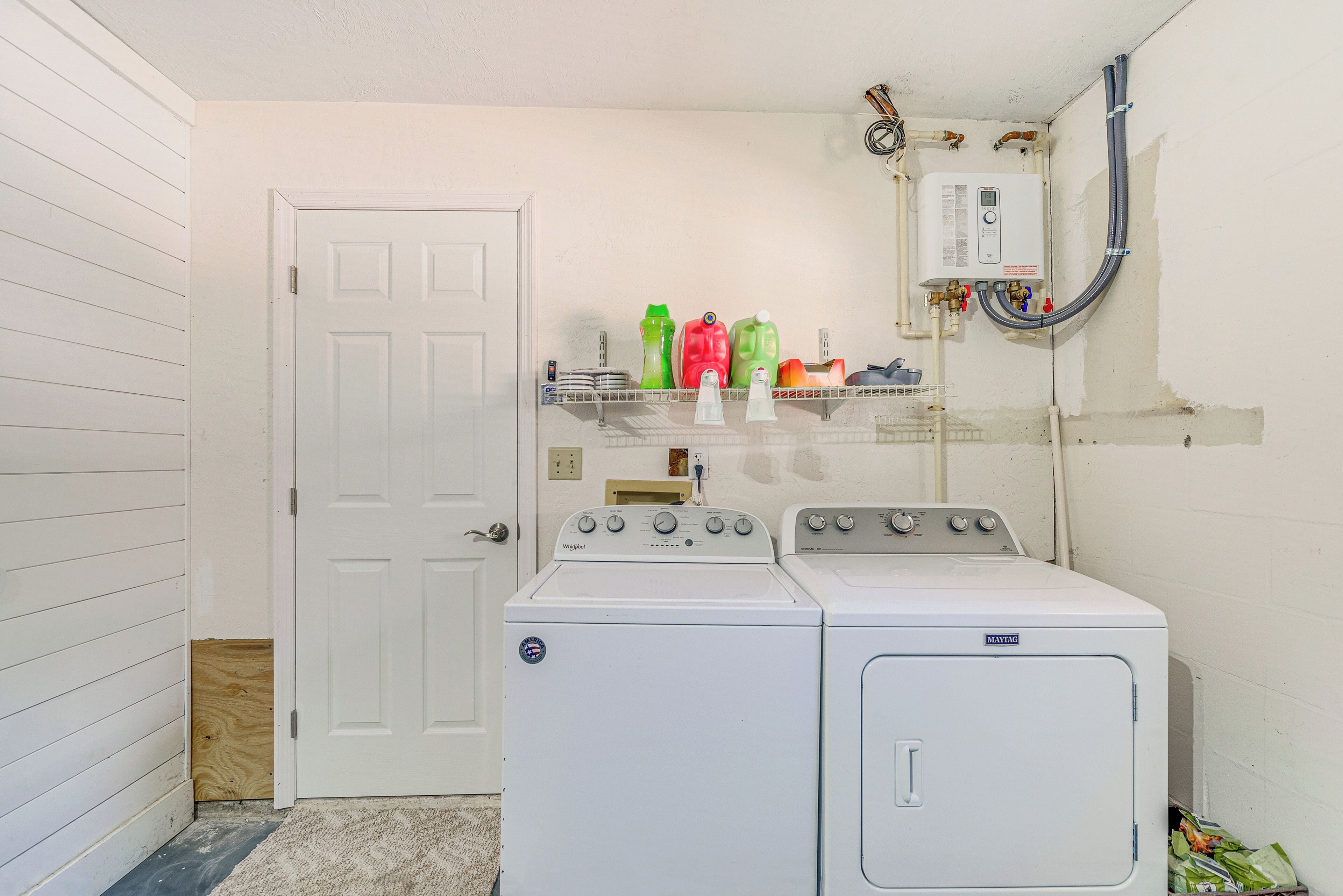 Une buanderie avec une porte blanche, un lave-linge et un sèche-linge, ainsi qu’une étagère contenant des produits de nettoyage.