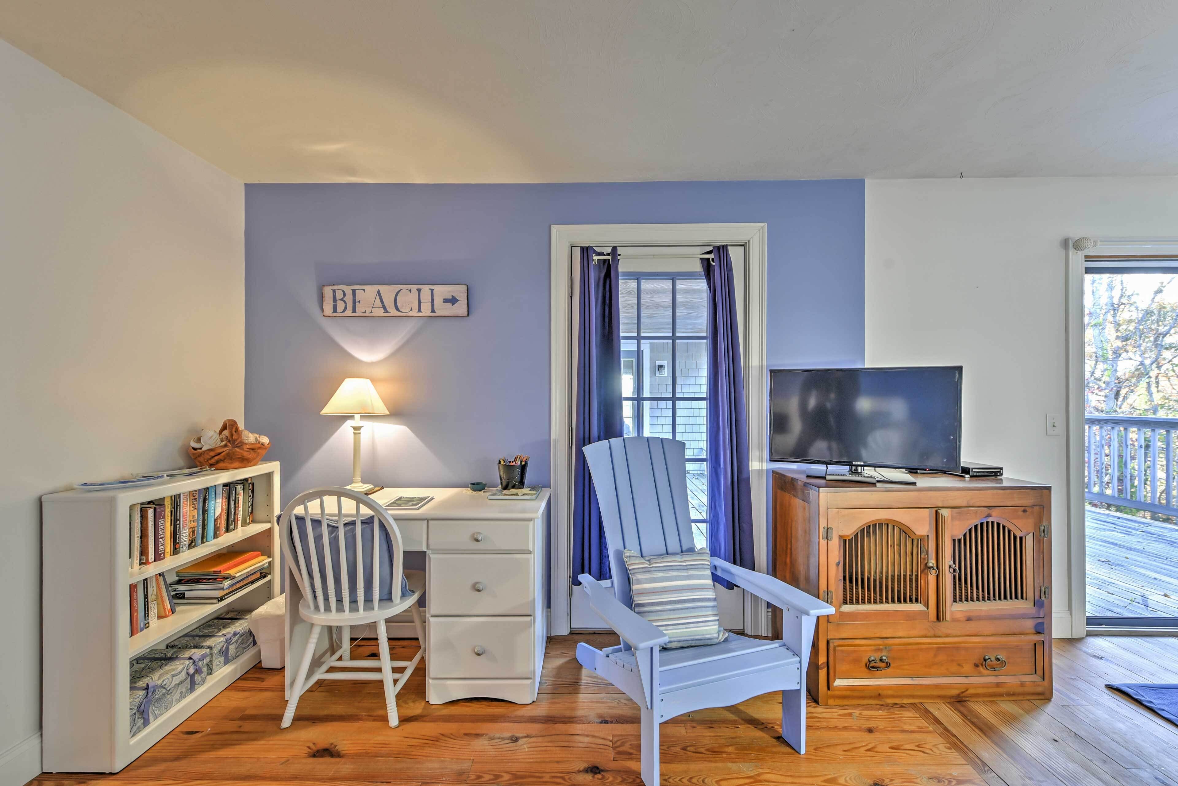 Une pièce confortable avec une bibliothèque, un bureau, une chaise, un téléviseur et un panneau indiquant « PLAGE ».