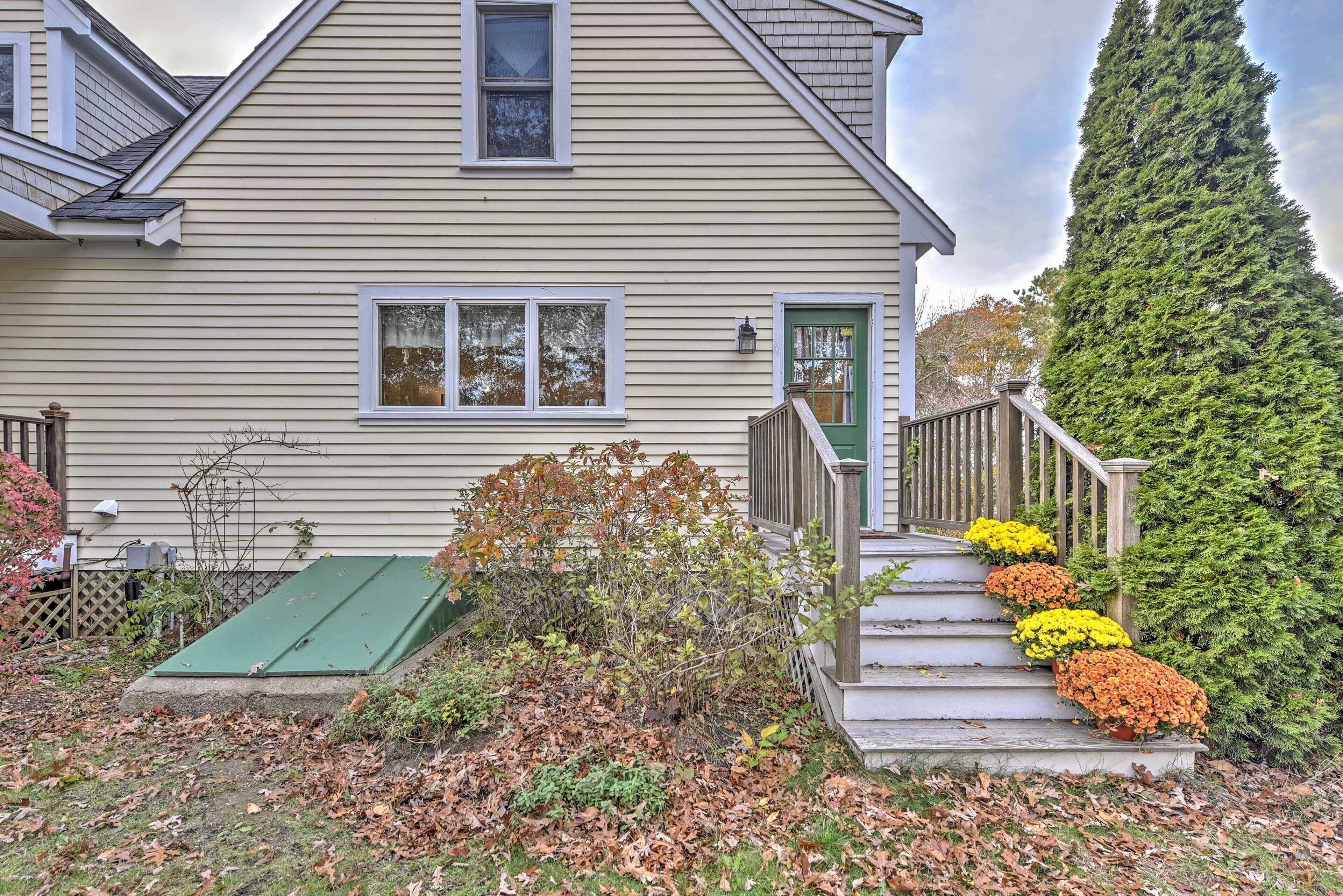 A two-story house with a green door, a small porch, and a staircase with colorful flowers.