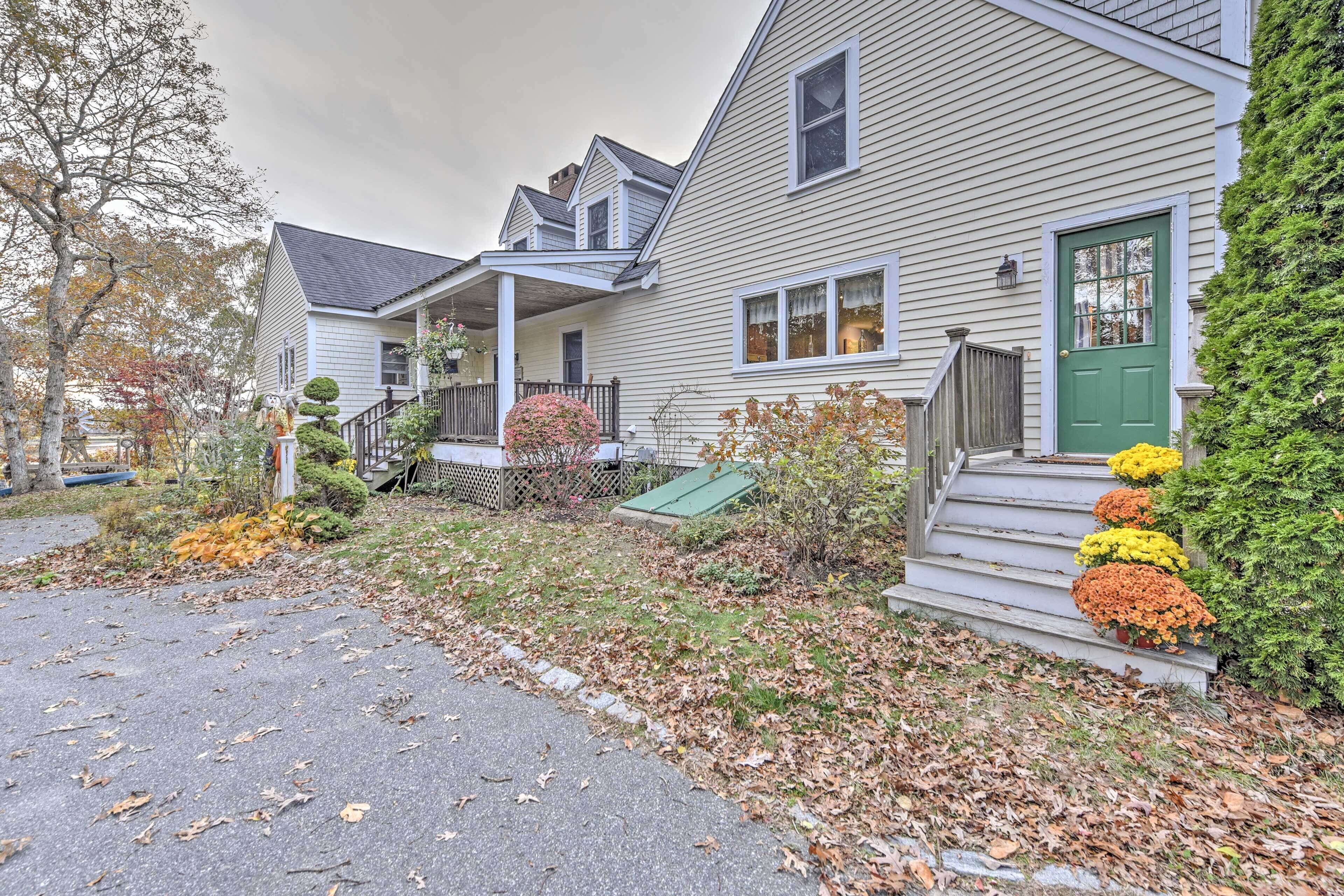 A two-story house with a porch, a green door, and a small garden with autumn leaves and flowers.
