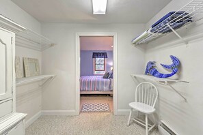 Un dormitorio con una cama, una silla, una estantería con objetos decorativos y una puerta que da a otra habitación.