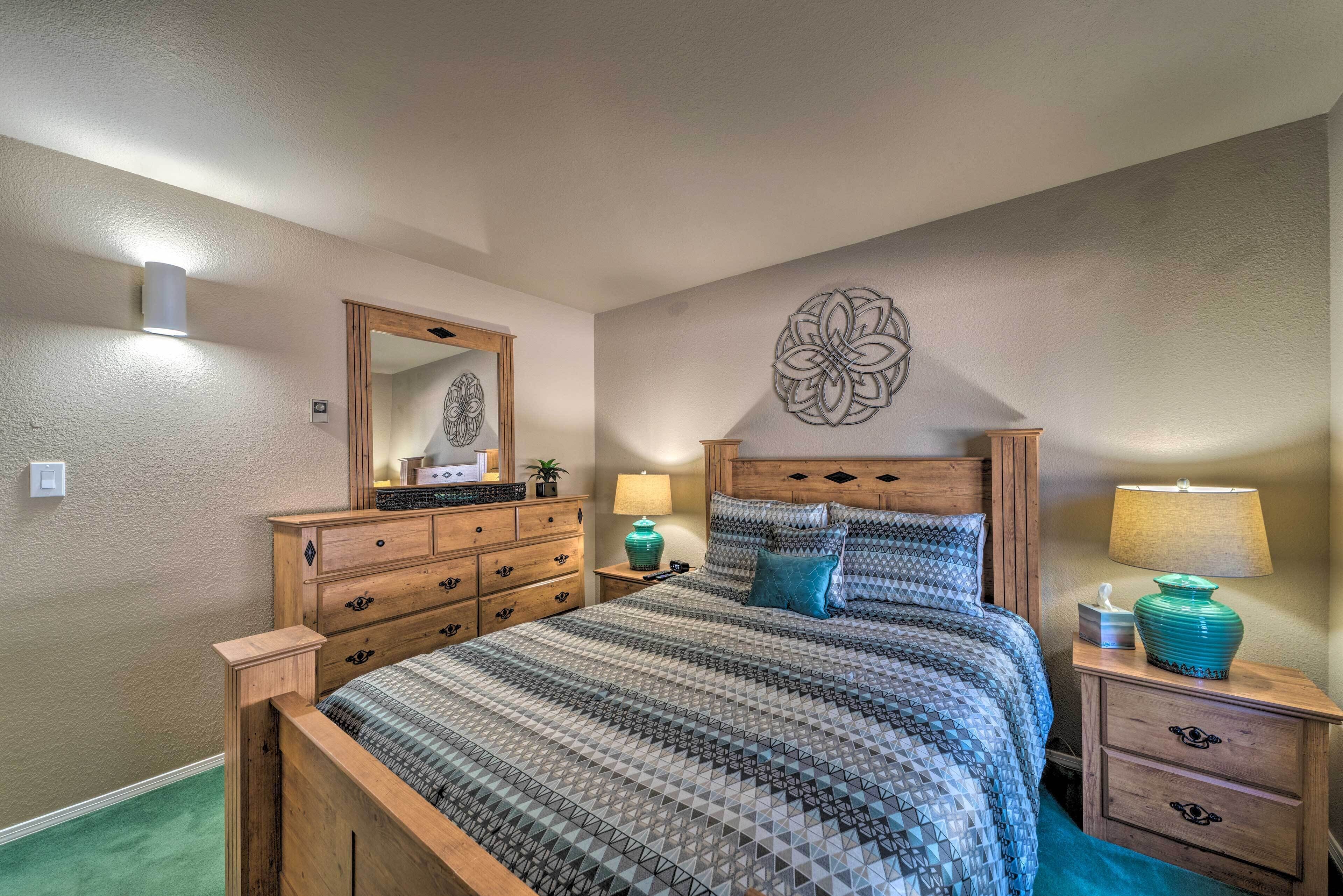 Een slaapkamer met een houten bed, een dressoir, een nachtkastje met een lamp en een wanddecoratie.