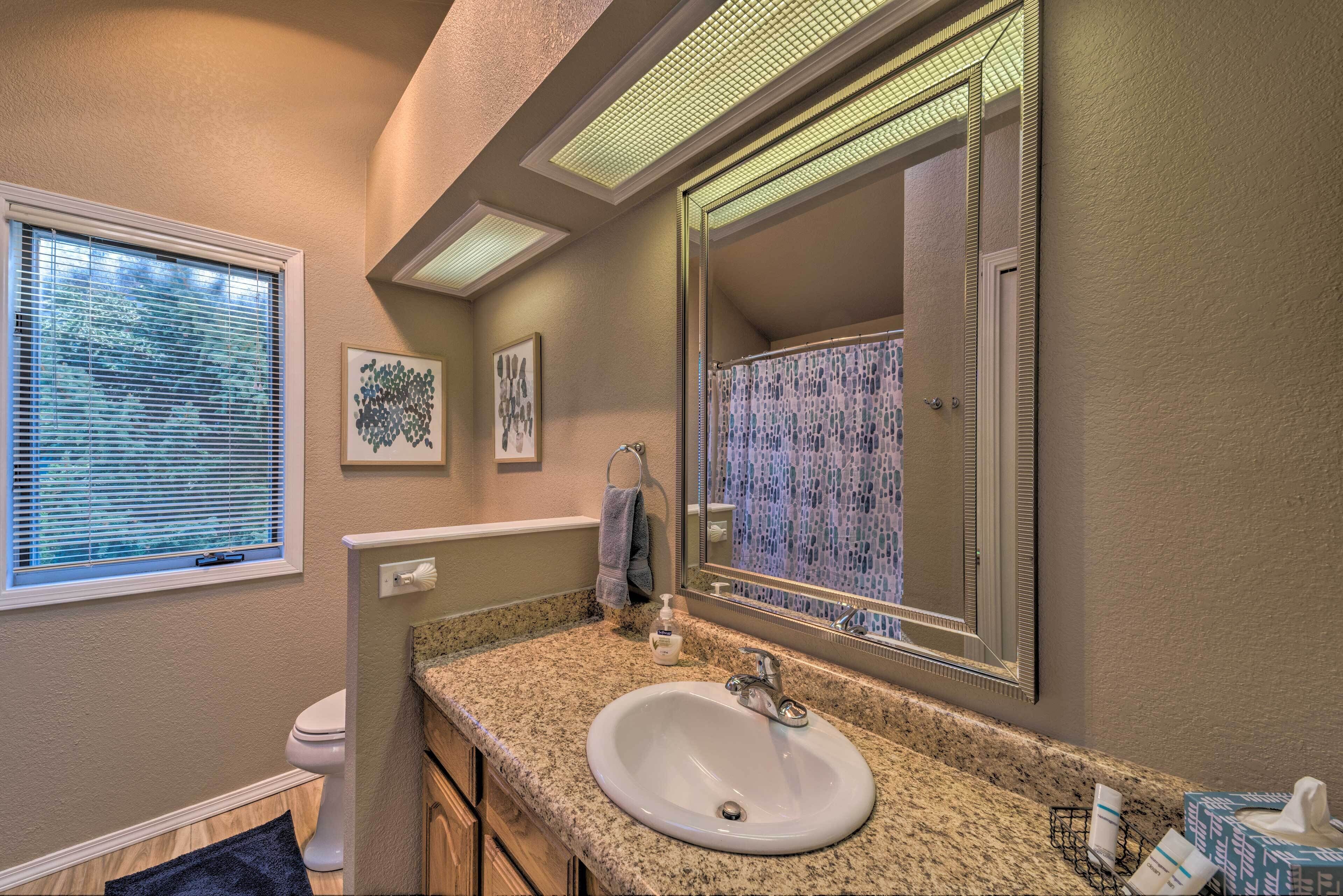 A bathroom with a granite countertop sink, a large mirror, and a window with blinds.