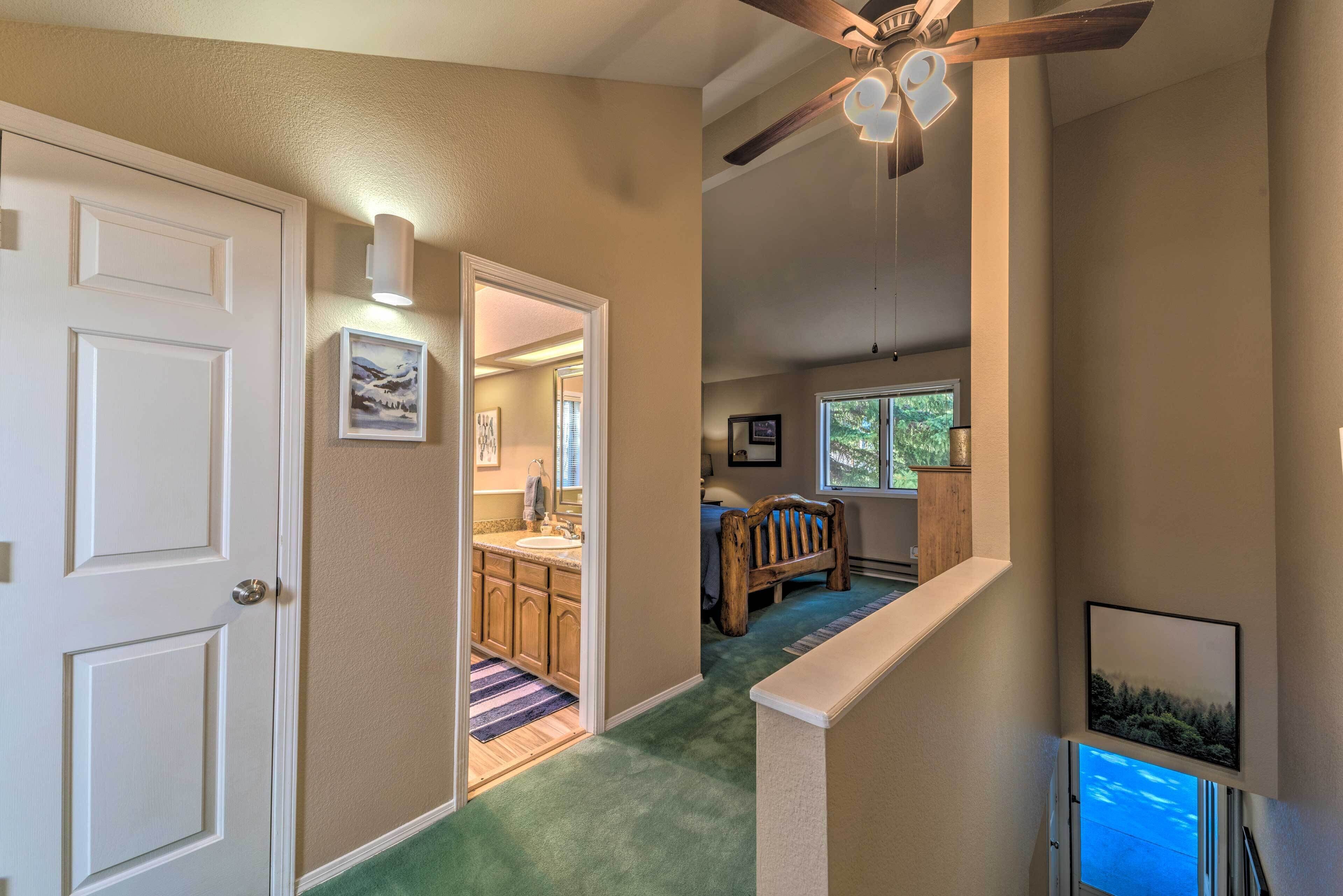 A hallway with a wooden bench, a ceiling fan, and a view of a bathroom with a sink and mirror.