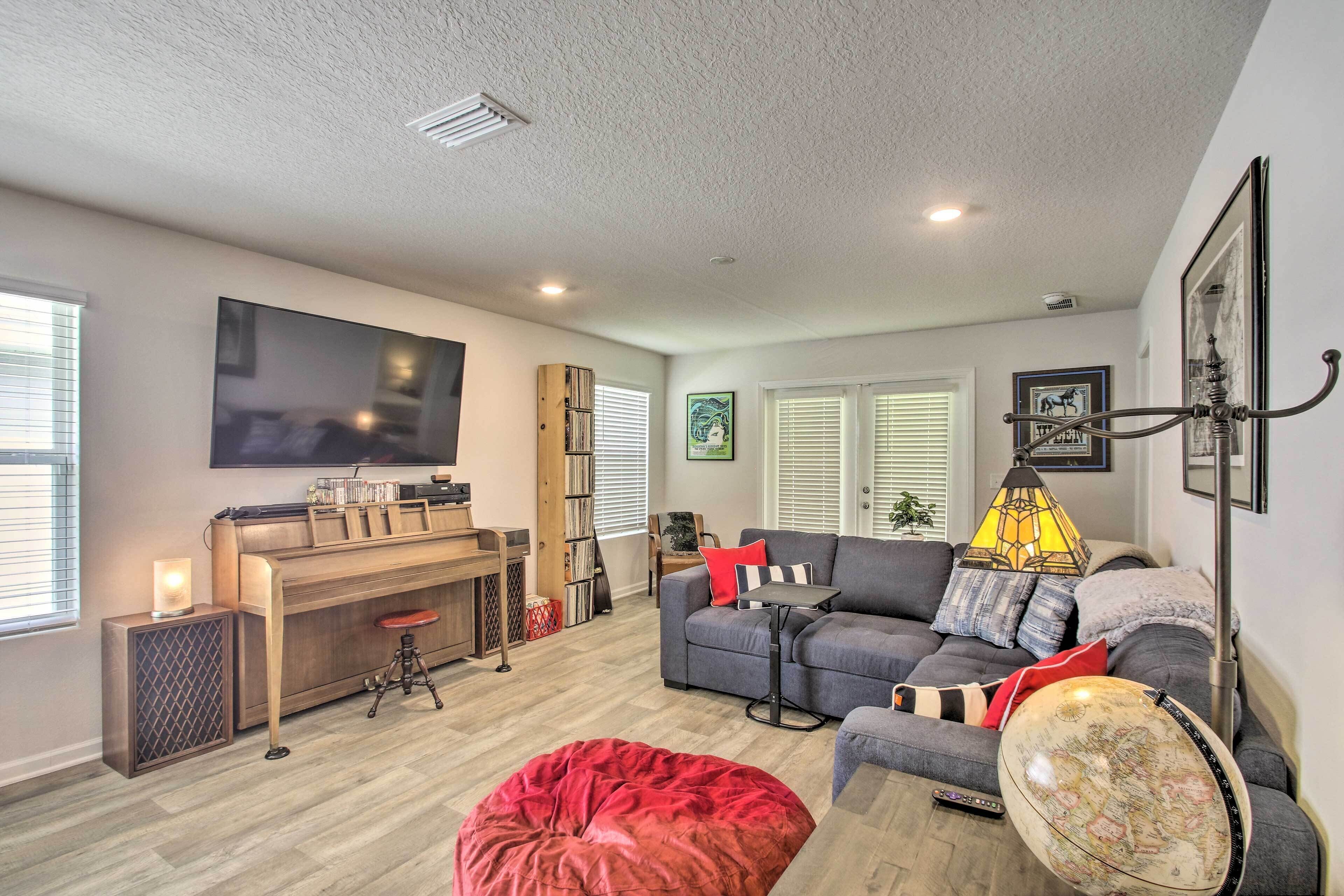 A living room with a flat-screen TV, a piano, a sofa, a red bean bag, and a lamp.