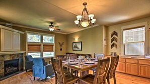 A dining area with a wooden table set for six, surrounded by six chairs. There is a fireplace with a stone surround, a ceiling fan, and a chandelier. - Redmond House w/ Community Amenities Access (Redmond)