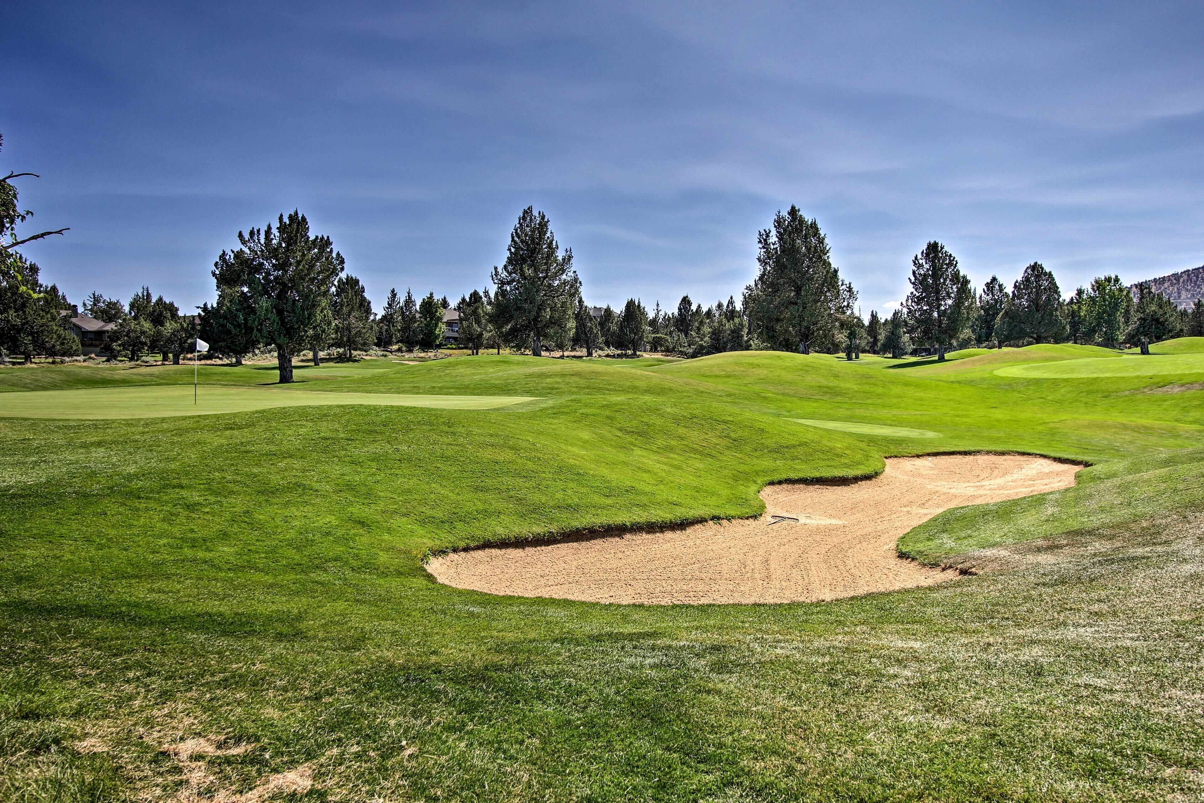A golf course with a sand bunker, trees, and a clear sky.