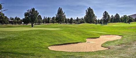 A golf course with a sand bunker, trees, and a clear sky.