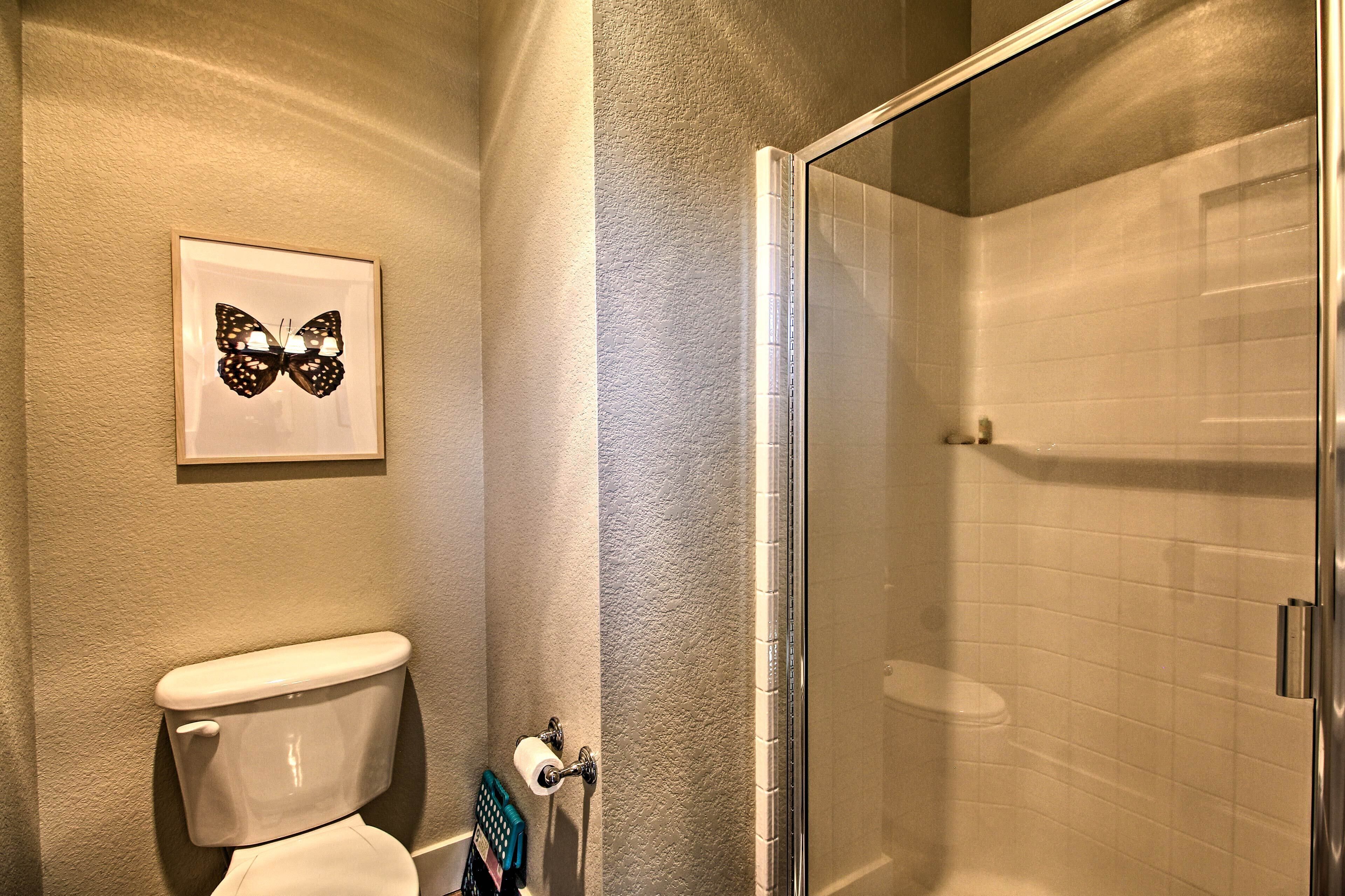 A bathroom with a toilet, a framed butterfly artwork, and a glass shower enclosure.