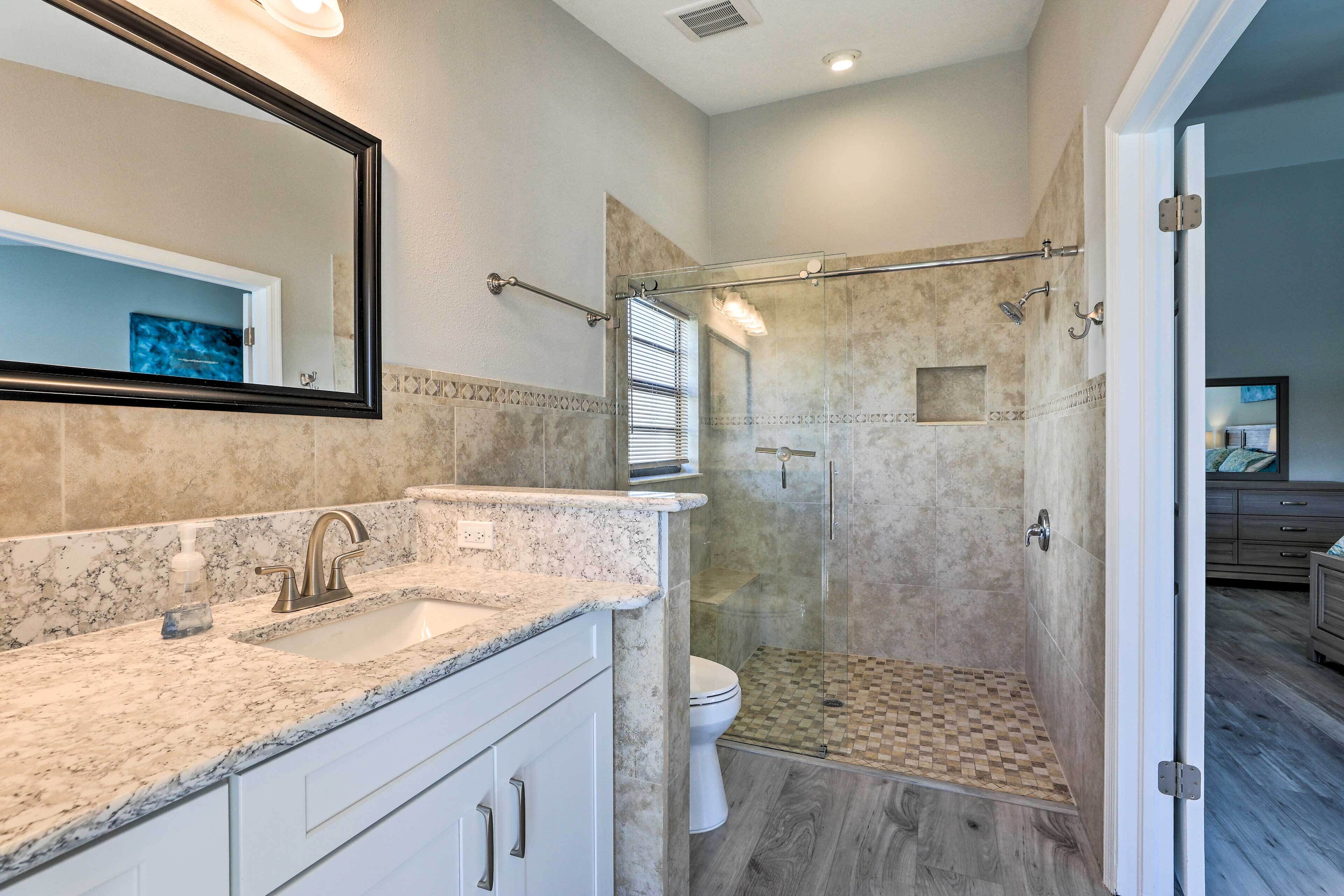 Un baño moderno con ducha de vidrio, lavamanos con encimera de mármol y un inodoro blanco.