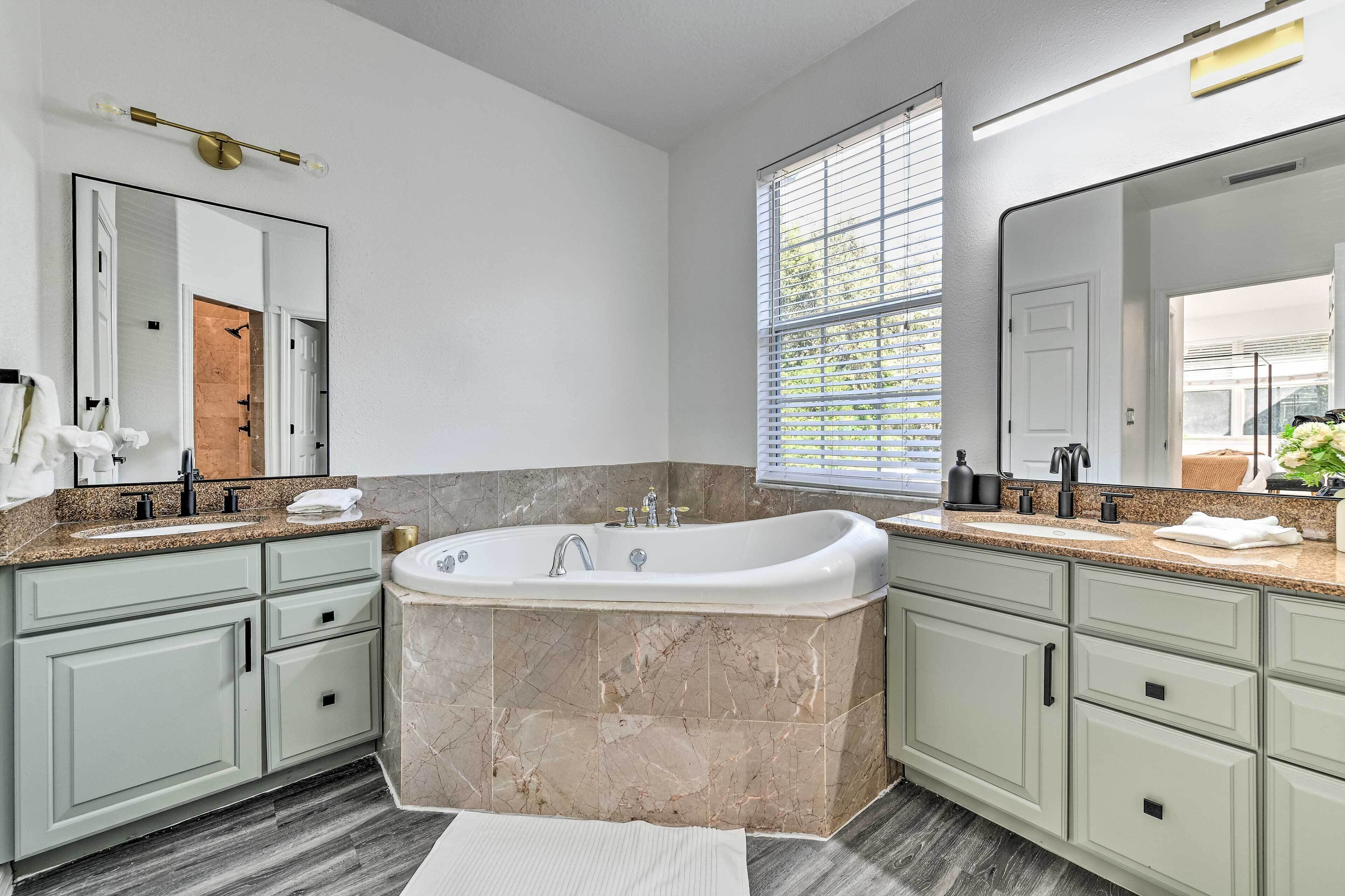 A modern bathroom with a freestanding bathtub, granite countertops, and light green cabinetry.
