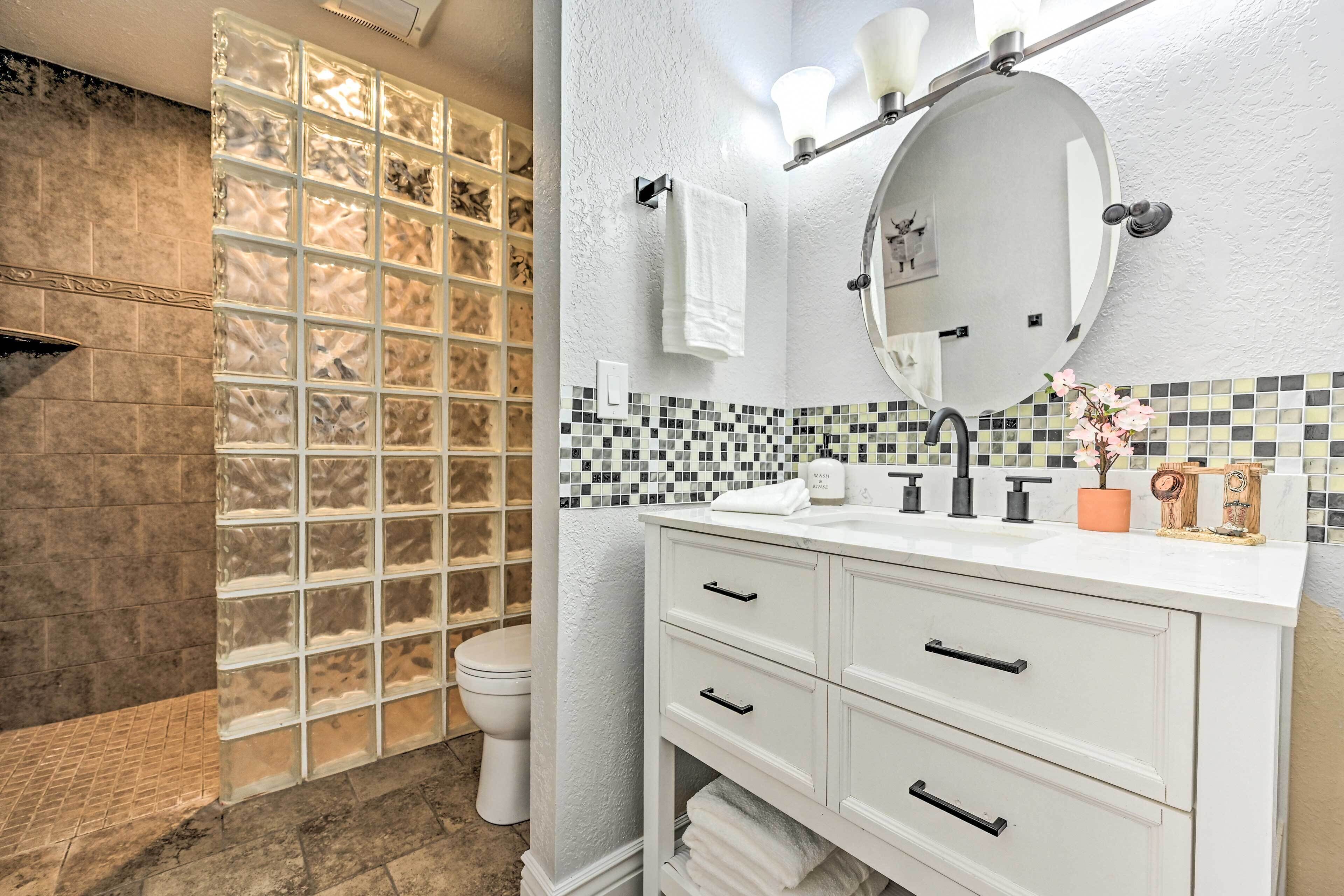 Une salle de bain avec une douche à parois de verre, un meuble-lavabo blanc avec un miroir et un mur recouvert de carreaux.