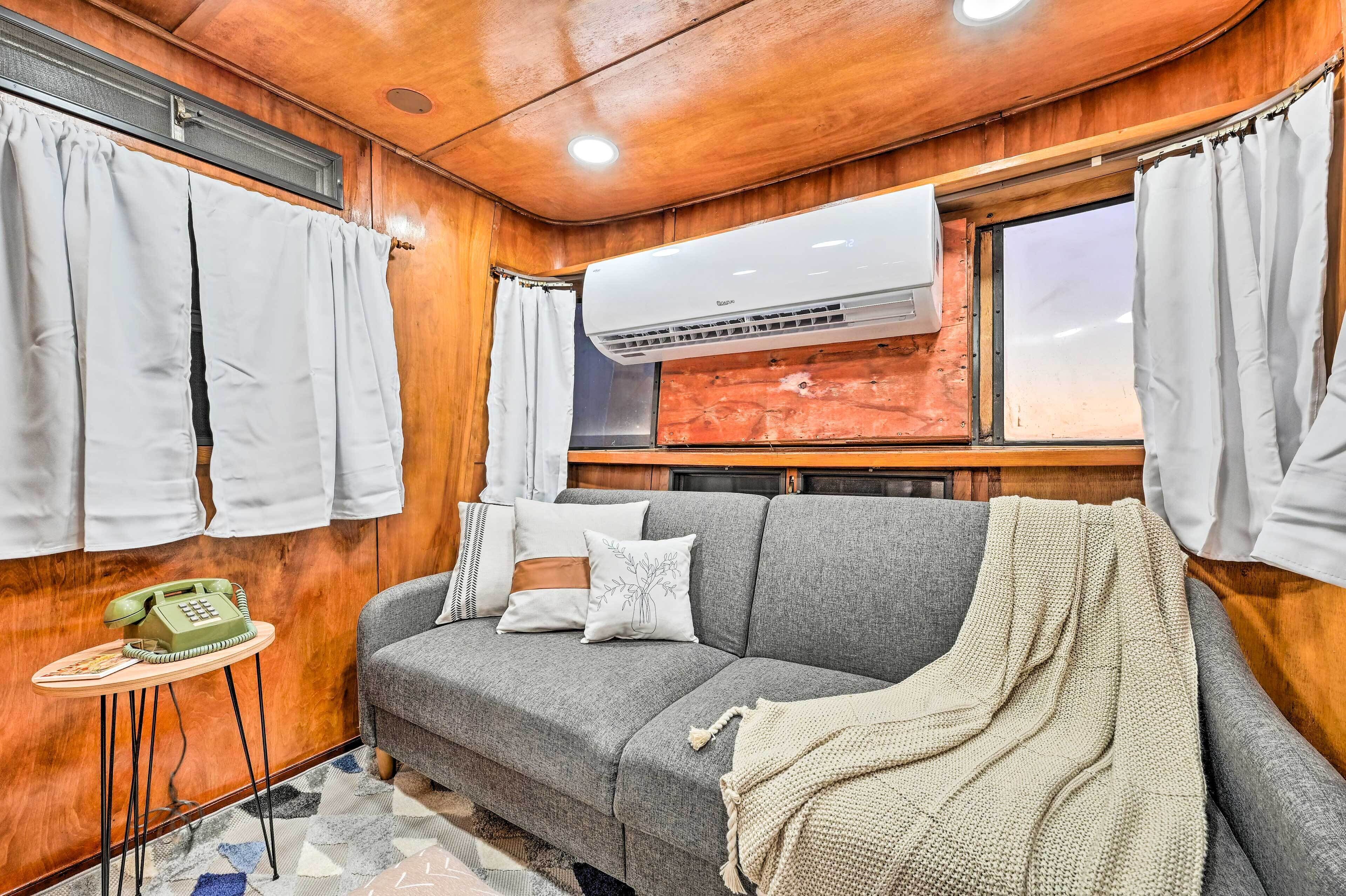A cozy room with a grey sofa, a small table with a telephone, and an air conditioning unit mounted on the wall.