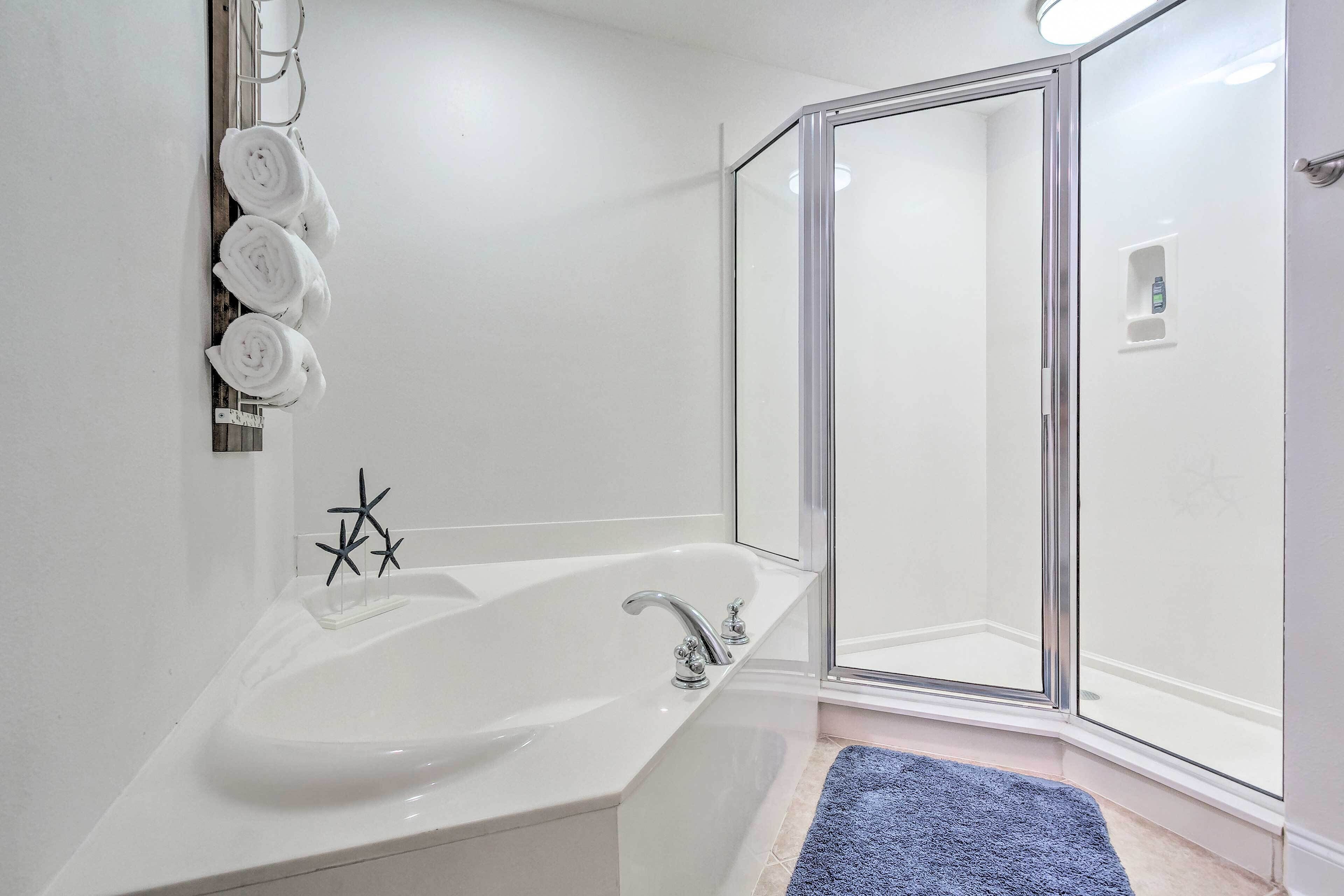 A modern bathroom with a bathtub, a glass shower enclosure, and a blue bath mat.