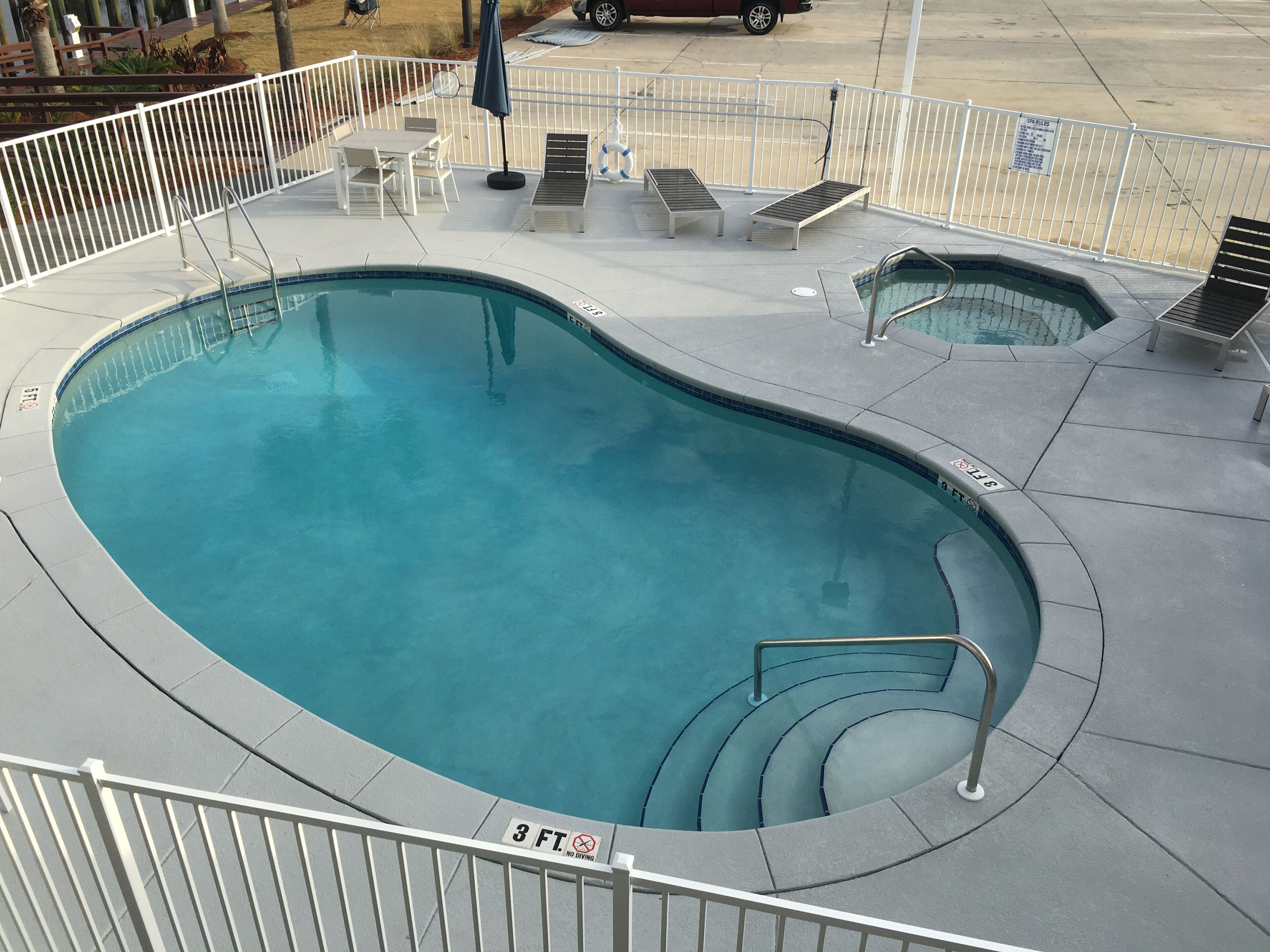 A swimming pool with a 3 ft no diving sign, lounge chairs, and a small deck area.