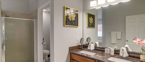 A bathroom with a shower, two sinks, a vanity, and a large mirror.