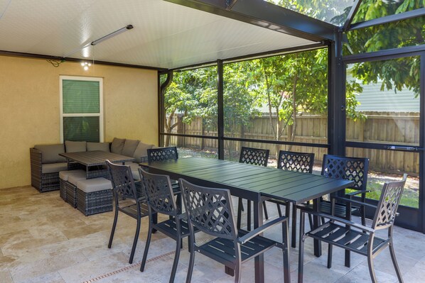 Un patio exterior con una mesa y sillas, un banco acolchado y vistas a una valla de madera y árboles.