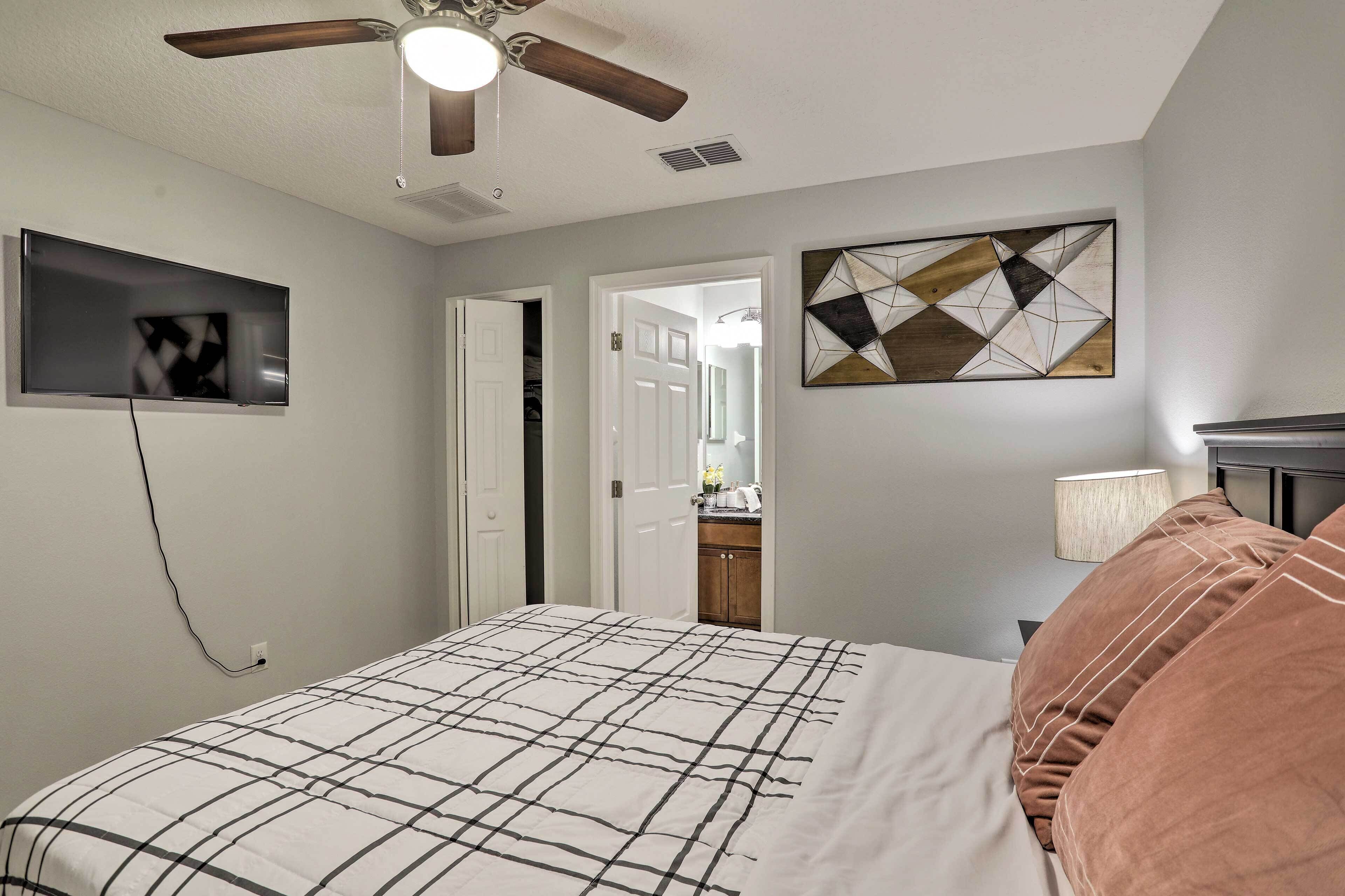 A bedroom with a bed, a ceiling fan, a TV mounted on the wall, and a door leading to a bathroom.