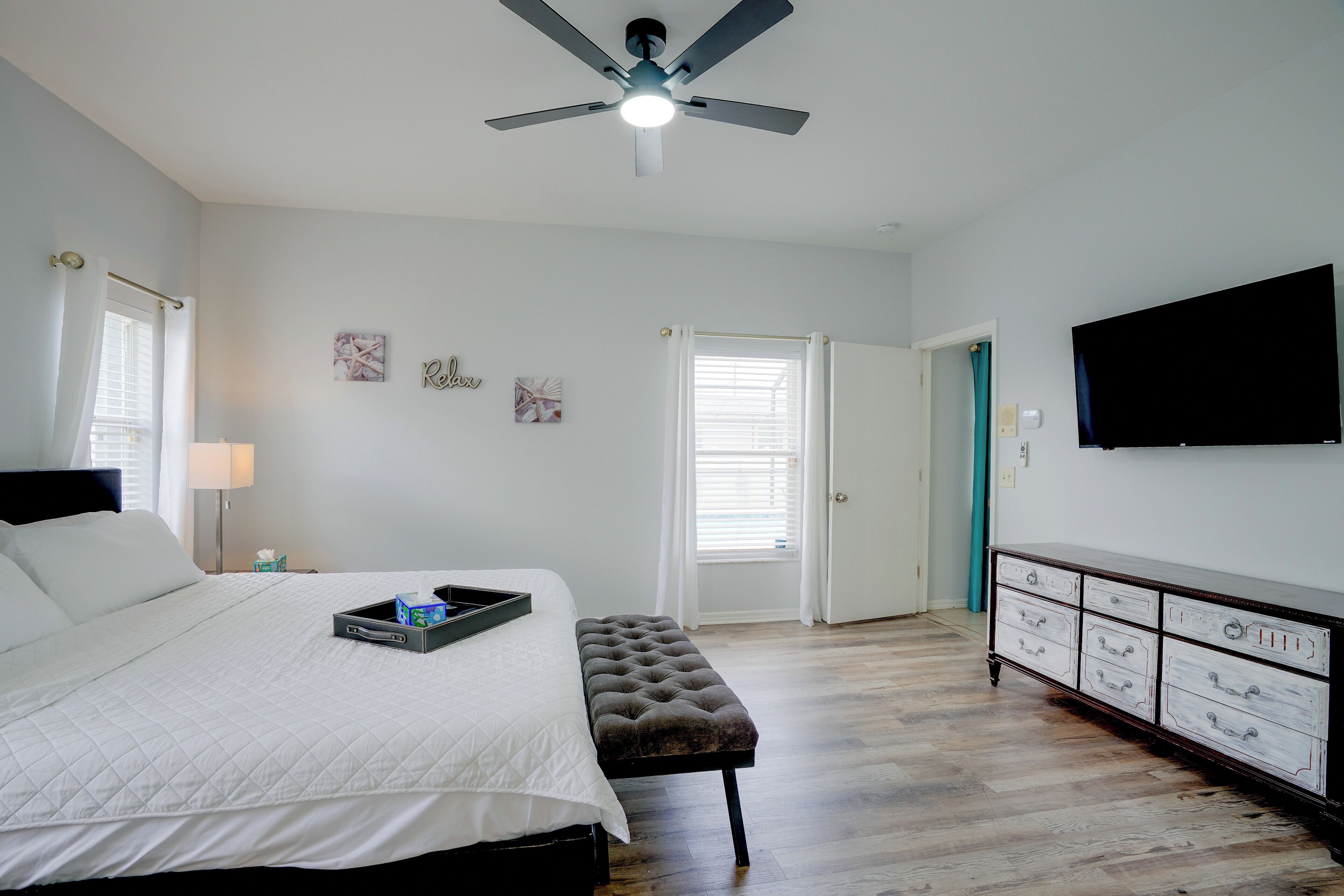 Une chambre à coucher avec un lit, un ventilateur de plafond, une commode et un téléviseur fixé au mur.