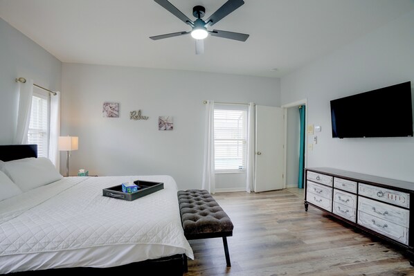 A bedroom with a bed, a ceiling fan, a dresser, and a television on the wall.