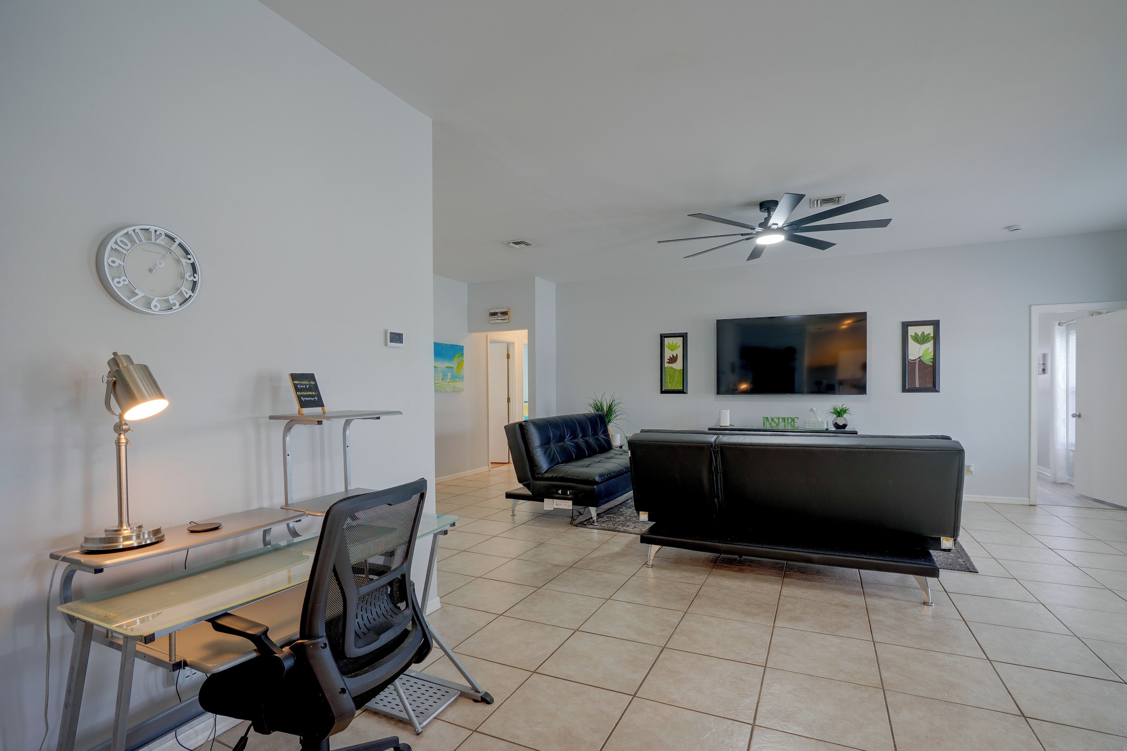 A modern living room with a desk, chair, sofa, and a ceiling fan.