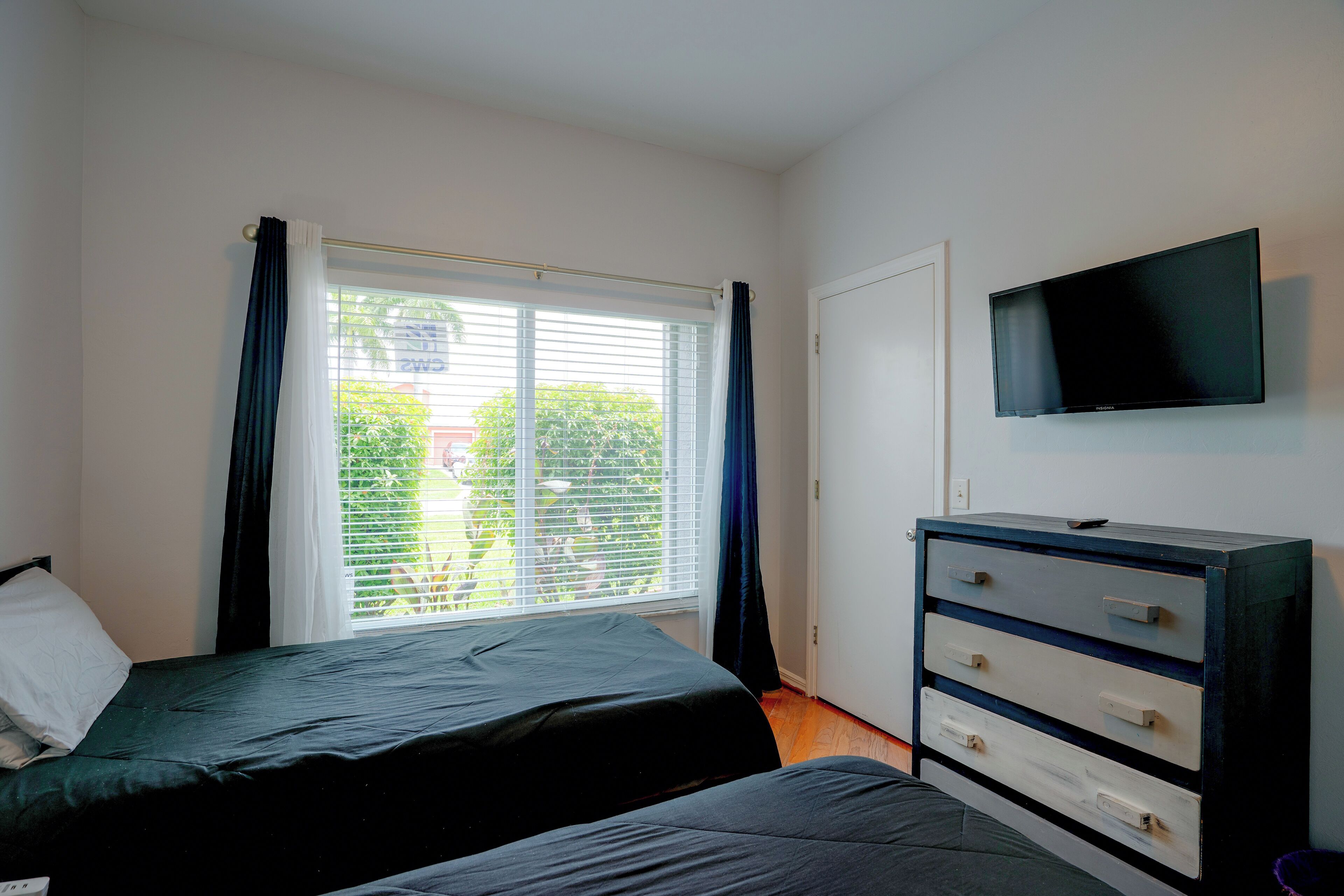A bedroom with a bed, a dresser, a television, and a window with blinds.