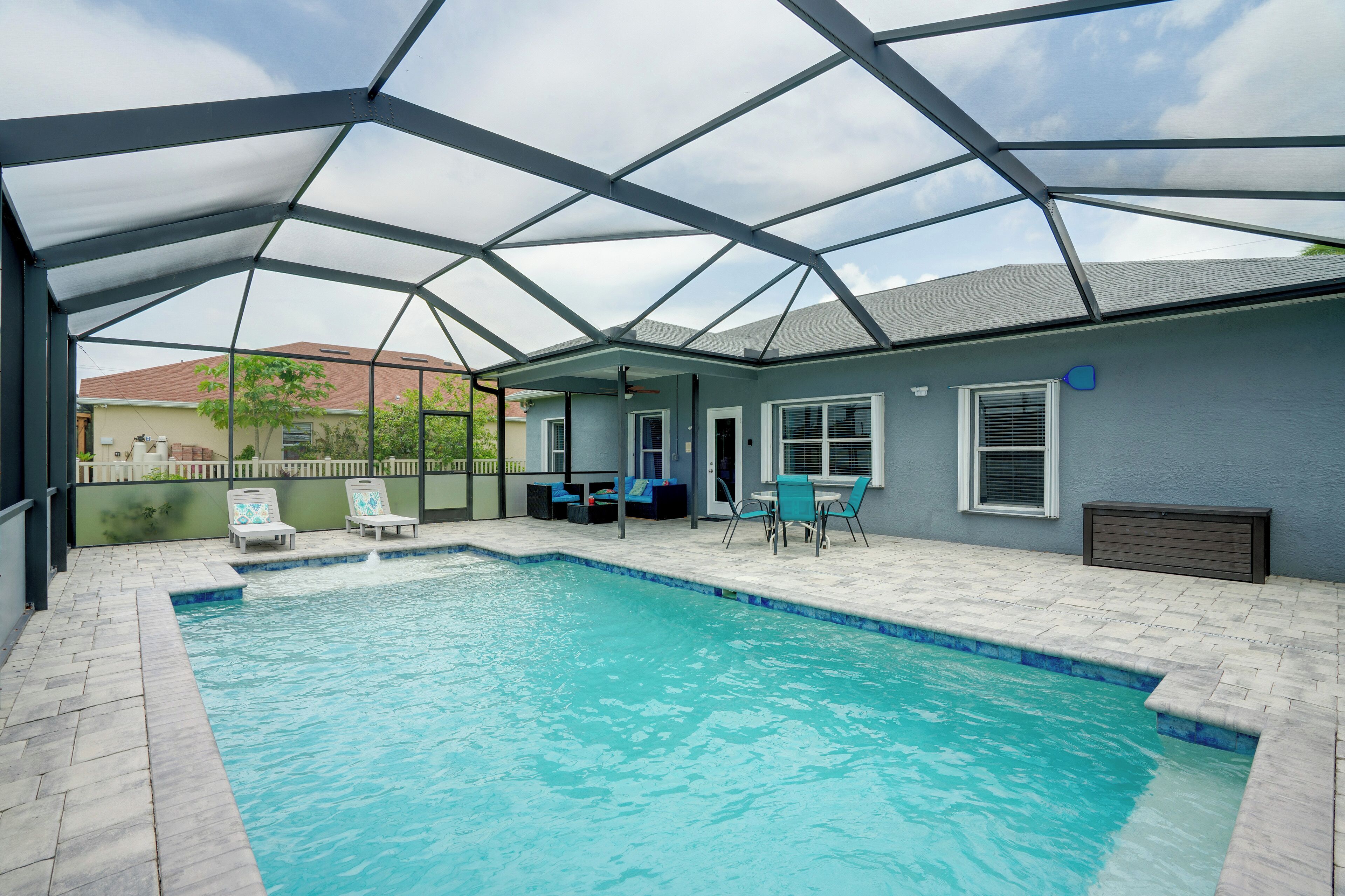 A covered swimming pool with lounge chairs and a table, surrounded by a patio area.