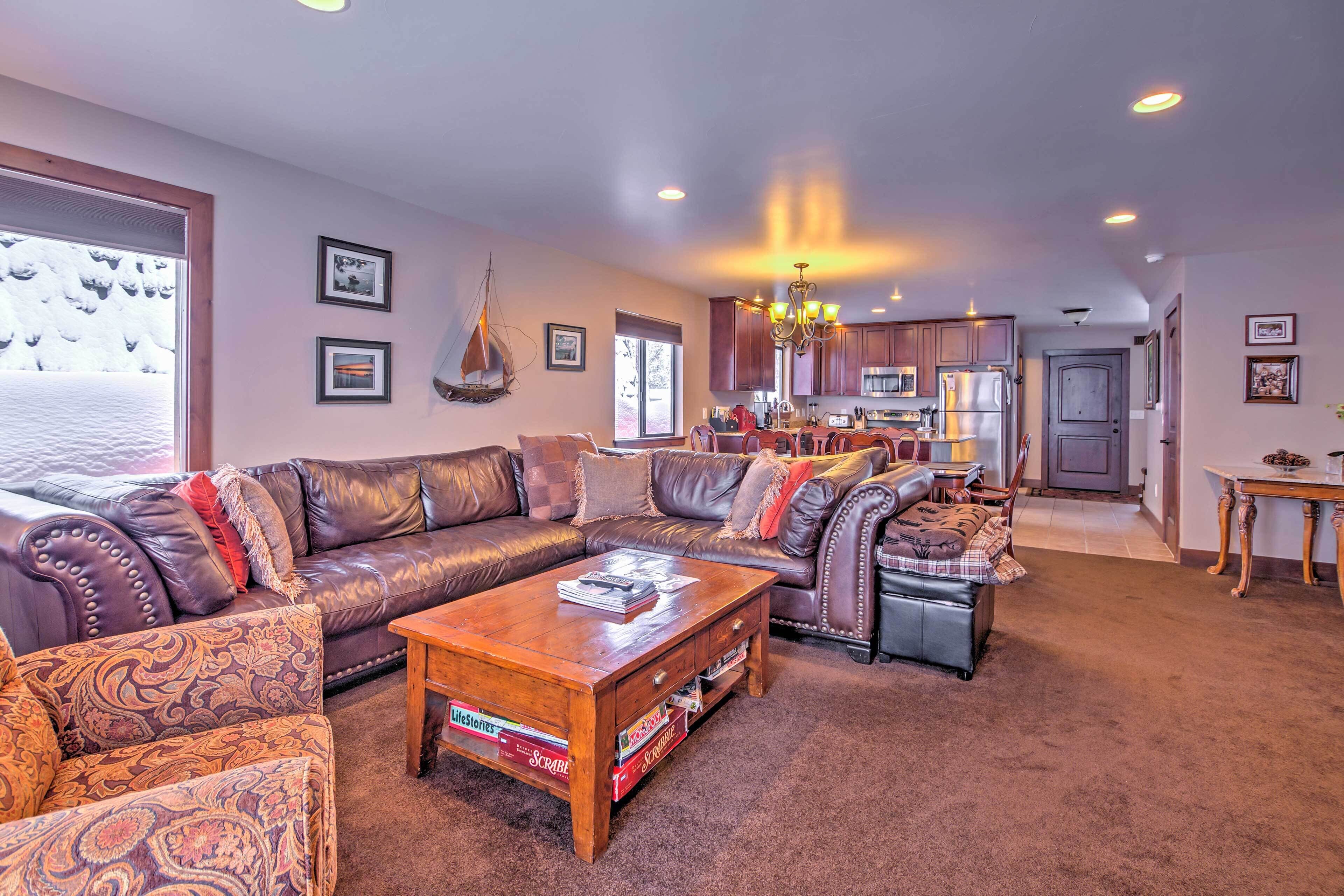A spacious living room with a leather sofa, a coffee table, and a dining area with wooden cabinets and a chandelier.