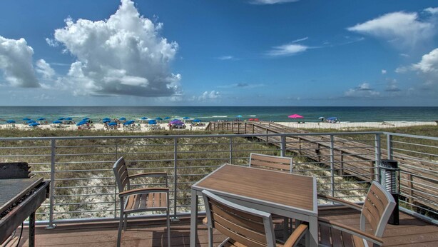 Una terrazza con tavolo e sedie che si affaccia su una spiaggia con ombrelloni e una passerella in legno.