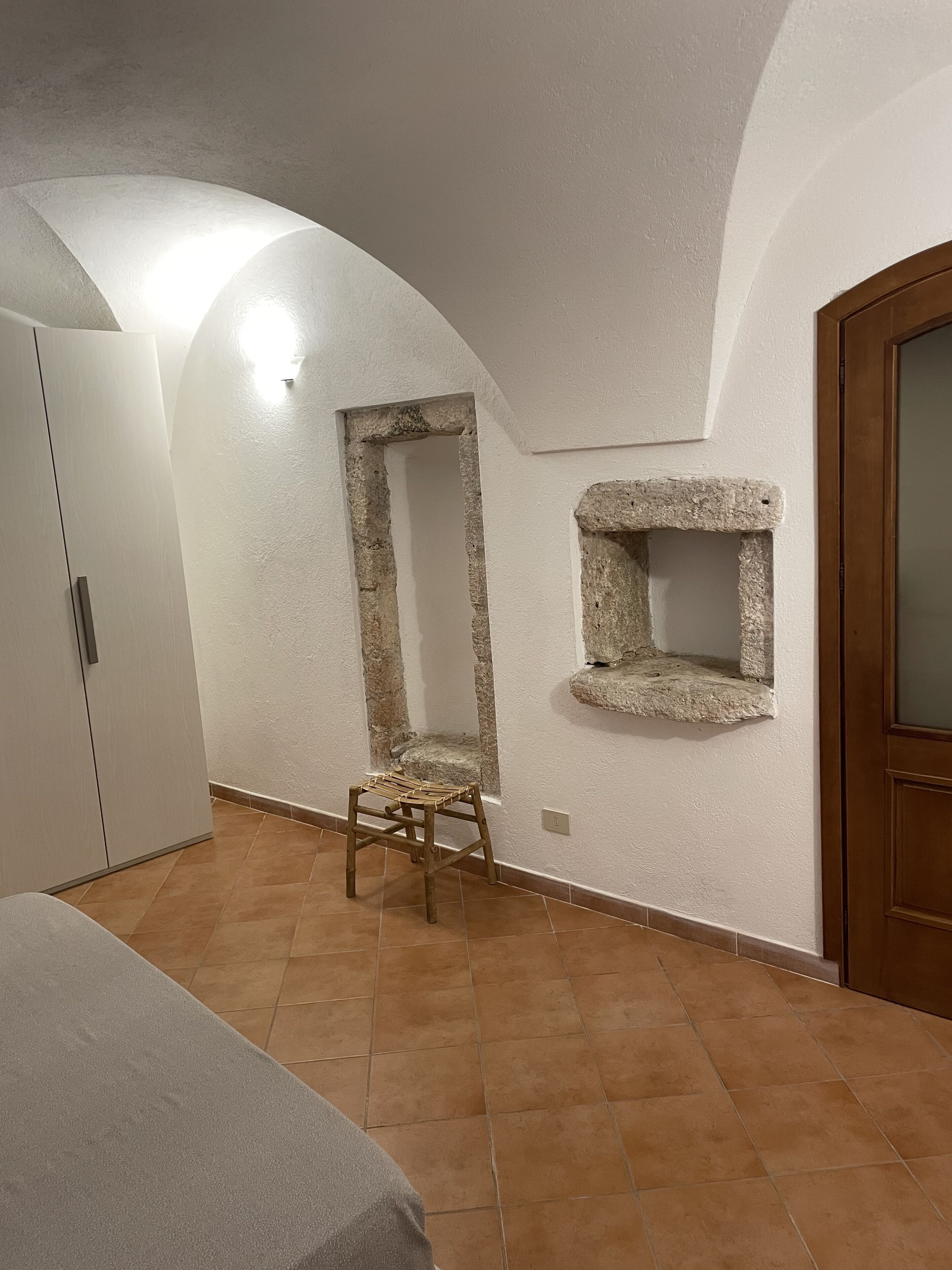 A room with a bed, a wardrobe, a small stool, and a stone shelf.