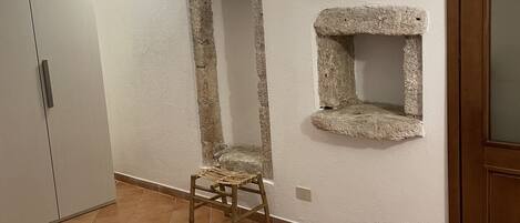 A room with a bed, a wardrobe, a small stool, and a stone shelf.