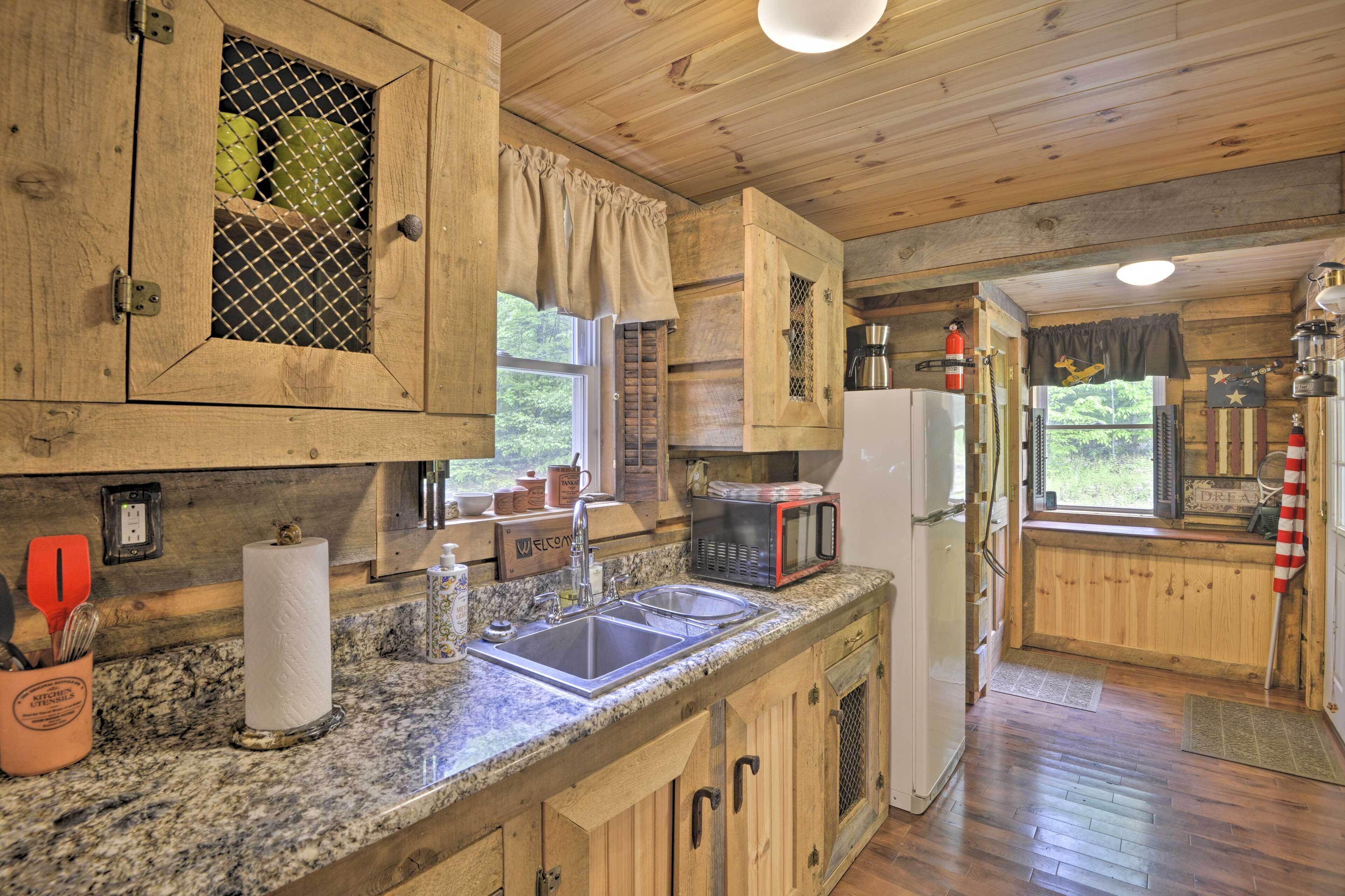 A rustic kitchen with wooden cabinets, a granite countertop, a sink, a microwave, and a refrigerator.