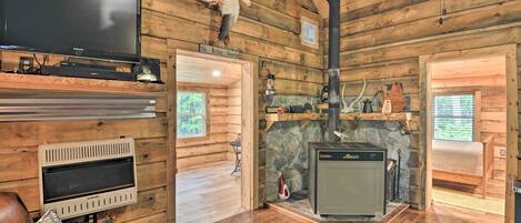 A log cabin interior with a stone fireplace, a flat-screen TV, leather furniture, and a sign reading "Sit Relax Gossip".