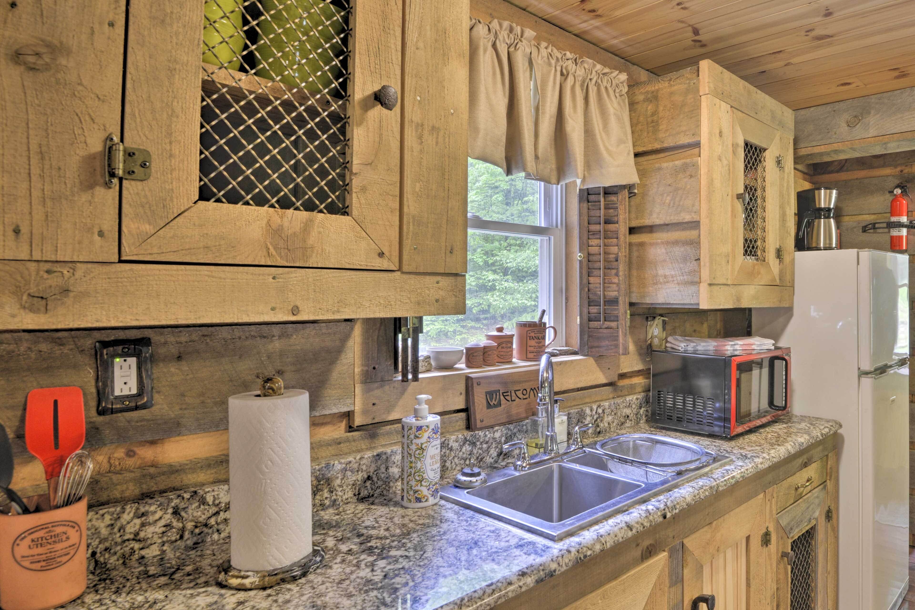 A rustic kitchen with wooden cabinets, a granite countertop, a sink, a microwave, and a coffee maker.