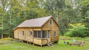 Une cabane en bois rustique, dotée d’un toit en métal, de grandes fenêtres et d’une véranda.