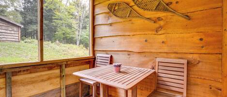 Une cabane en bois avec une table et deux chaises, une raquette de tennis et un petit drapeau américain décoratif.