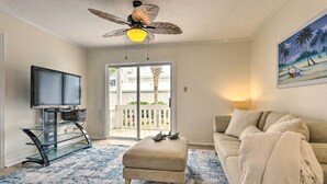 Ein Wohnzimmer mit Fernseher, Glastrennwänden, Deckenventilator, einer Couch und einem Gemälde.