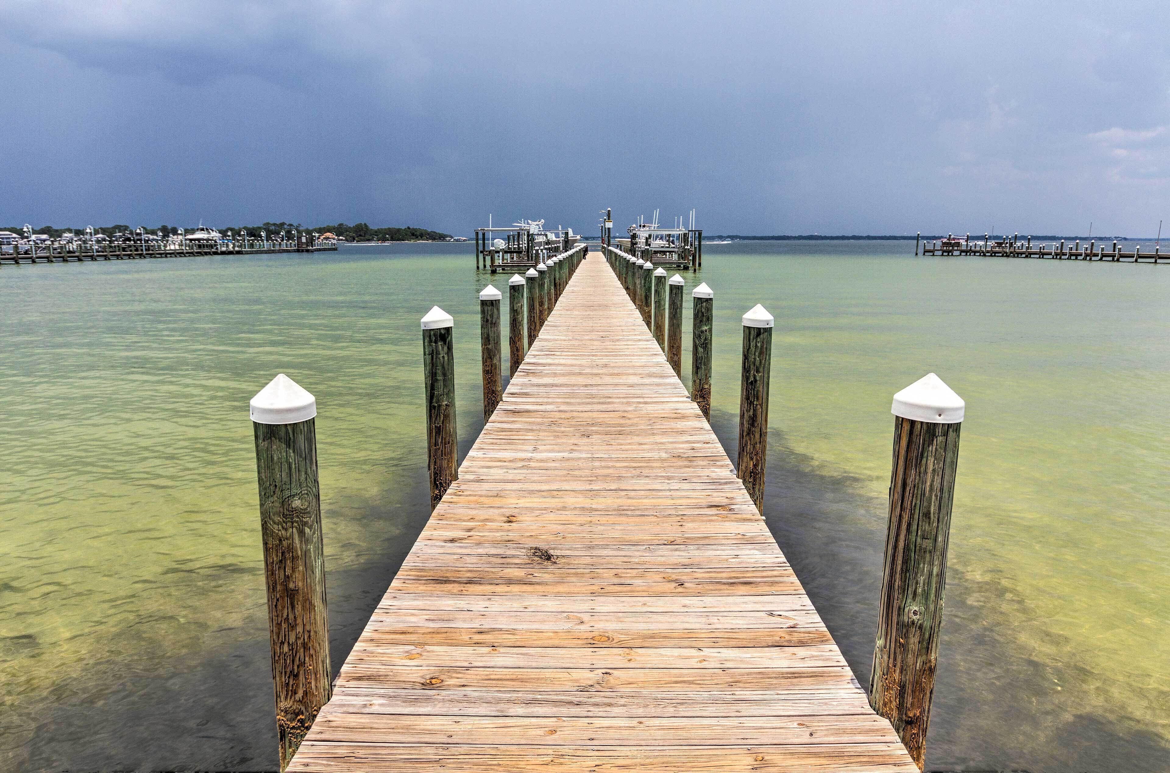 Un muelle de madera se extiende sobre el agua, con aguas cristalinas a un lado y un área de amarre para barcos al otro.