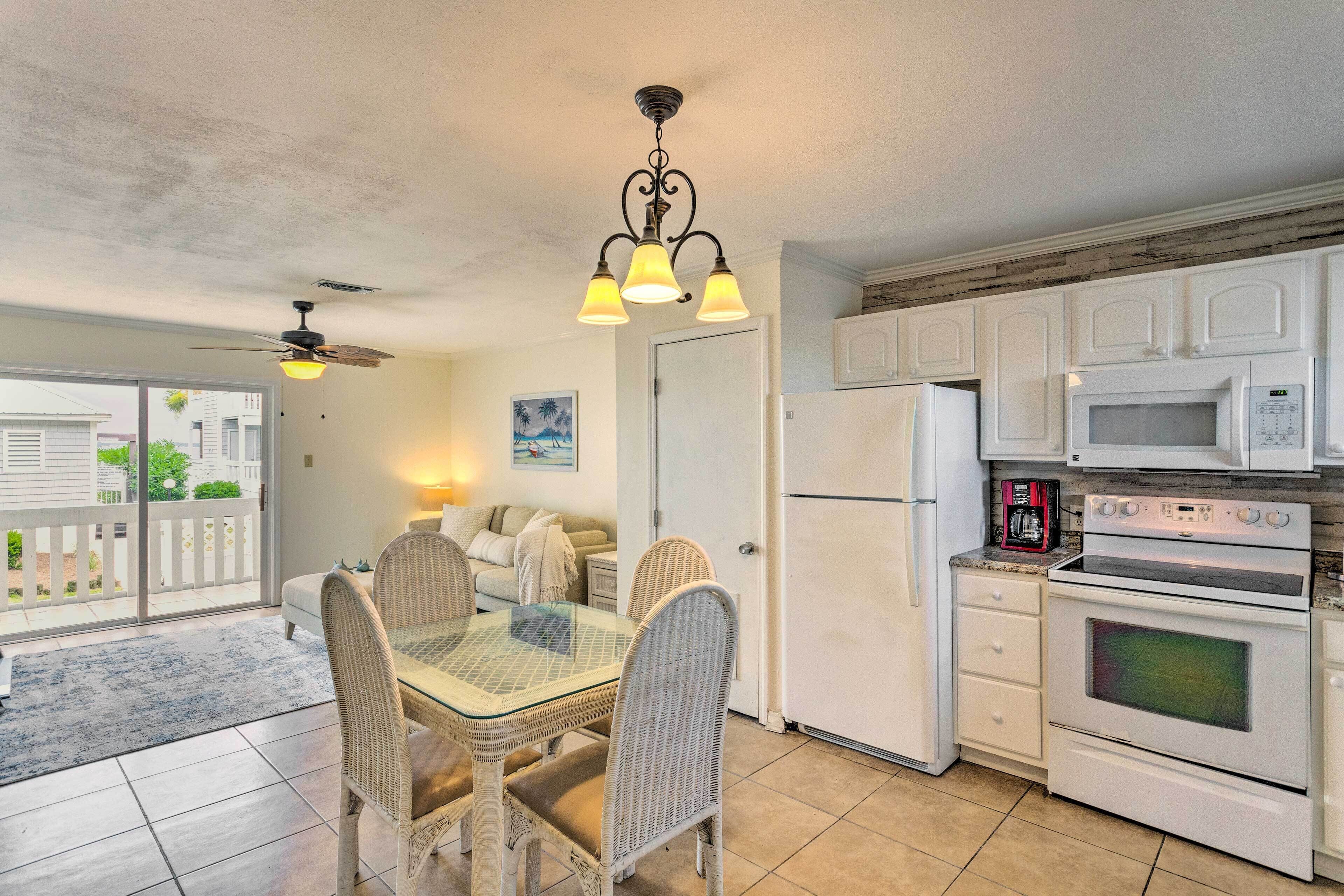 A kitchen with white cabinets, a microwave, an oven, and a dining area with wicker chairs and a glass table.