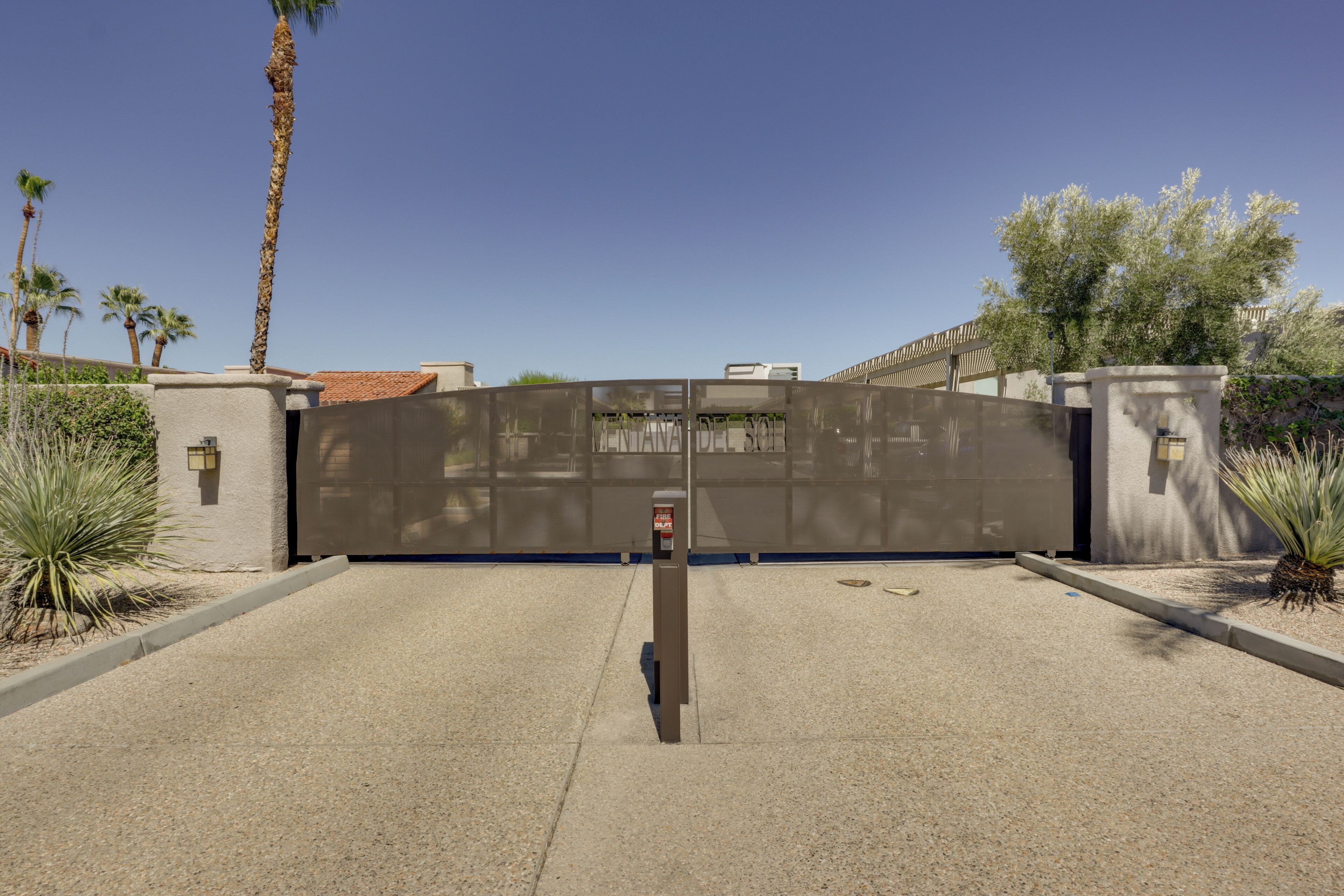 A gated entrance with a fire department sign, palm trees, and a clear sky.