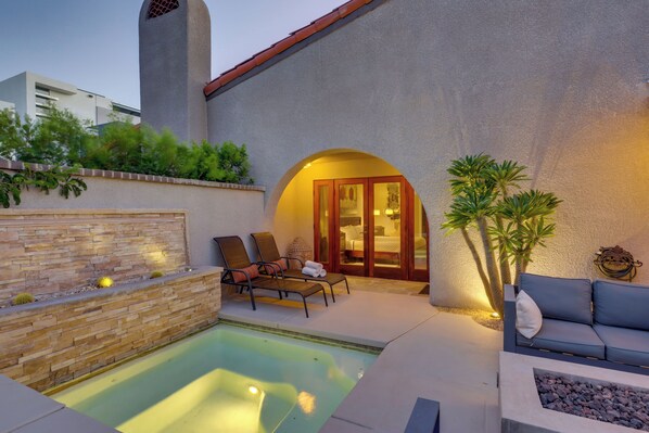 A pool area with a stone wall, lounge chairs, and a door leading to a bedroom.
