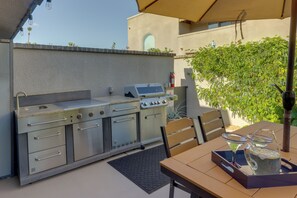 An outdoor kitchen with a grill, oven, and sink, a table with chairs, and a fire extinguisher.